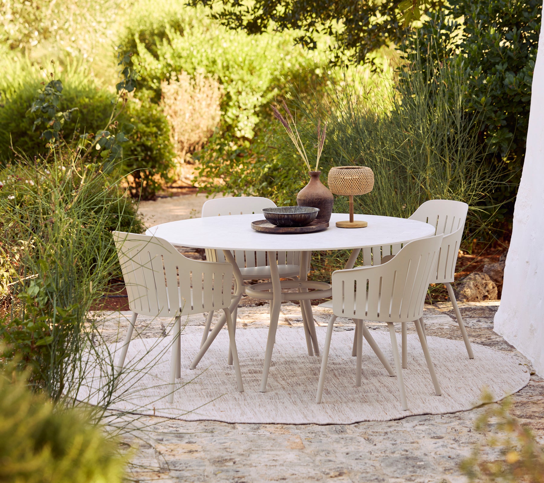 Gartenmöbelset mit einem weißen runden Tisch und beigen Stühlen, umgeben von Grün.