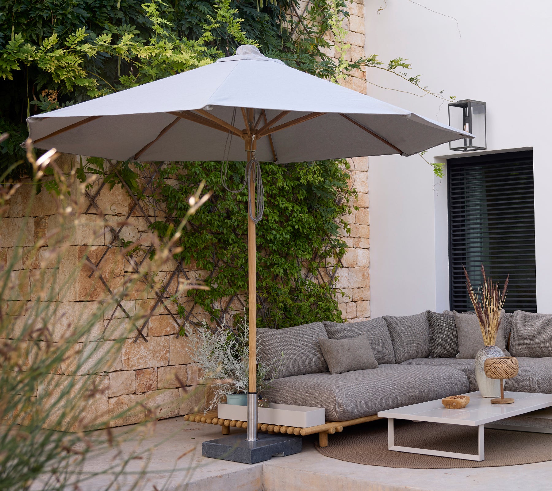 Moderne Loungebereich mit einem grauen Sofa, einem weißen Tisch und einem grauen Sonnenschirm.