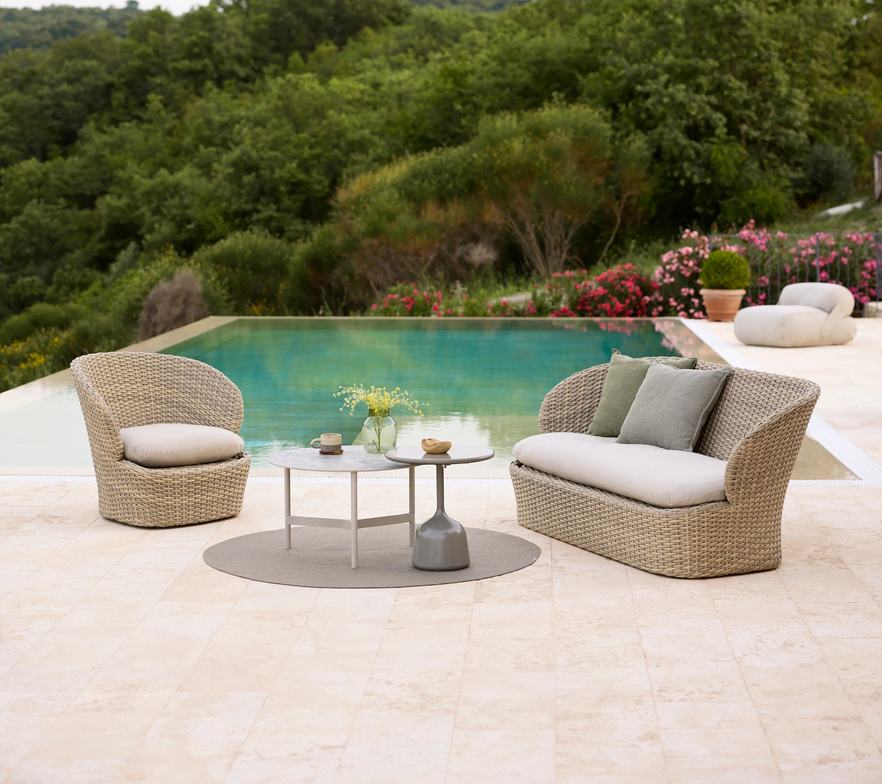 Küsten-Lounge-Sitzmöbel mit weichen Kissen, kombiniert mit einem Twist-Teetisch und einem Glaze-Teetisch, umgeben von üppigem Grün und einem Pool.