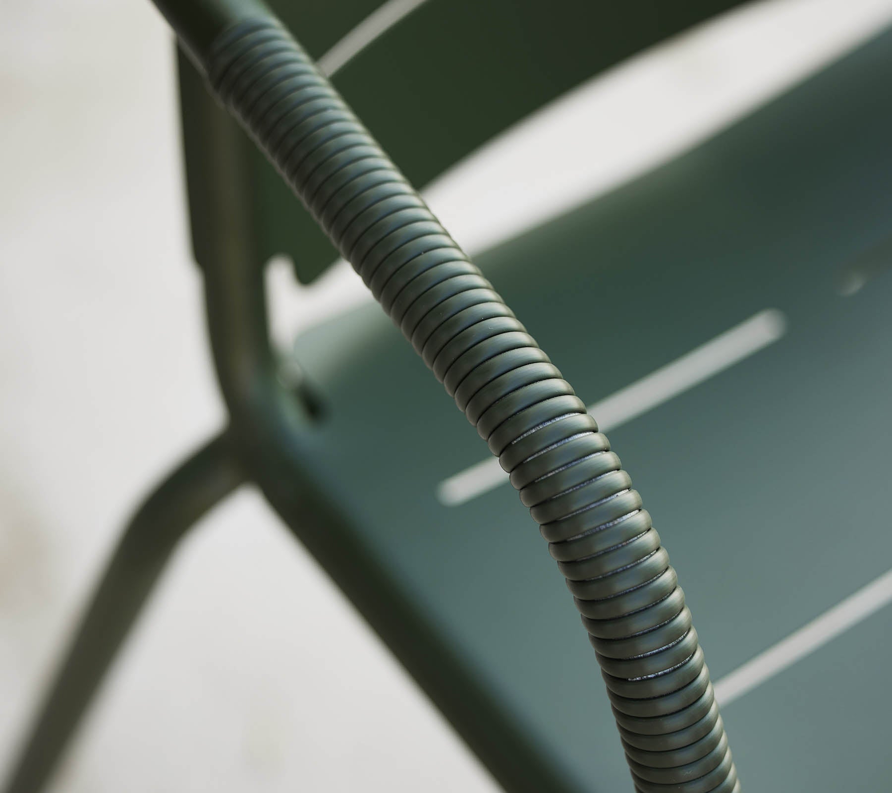 Nahaufnahme eines grünen Copenhagen-Stuhls, der die gebogene Armlehne und das schlanke Design mit subtilen Rillen auf dem Sitz hervorhebt.