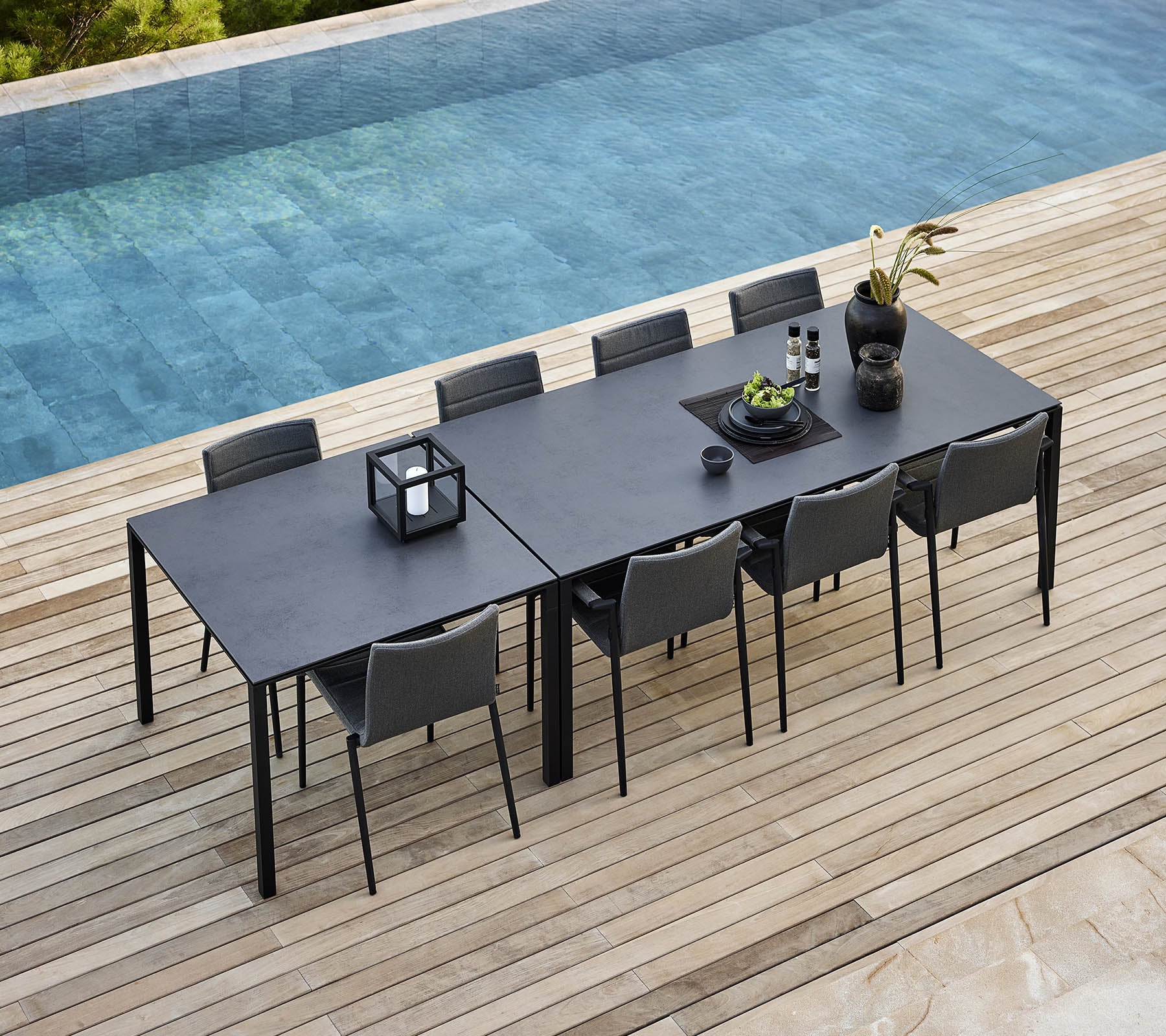 Ein elegantes Esszimmer-Setup mit einem schlichten Tisch und modernen Stühlen, geschmückt mit dekorativen Pflanzen und Accessoires neben einem ruhigen Pool.