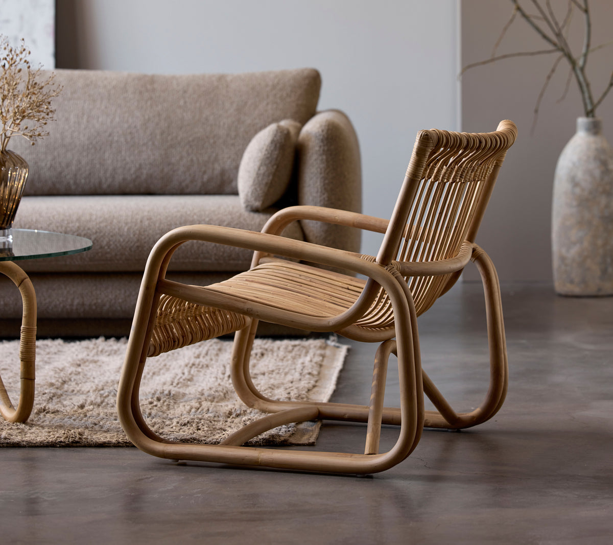 Rattanstuhl neben einem beigen Sofa und einem Glastisch in einem modernen Lounge-Setting.
