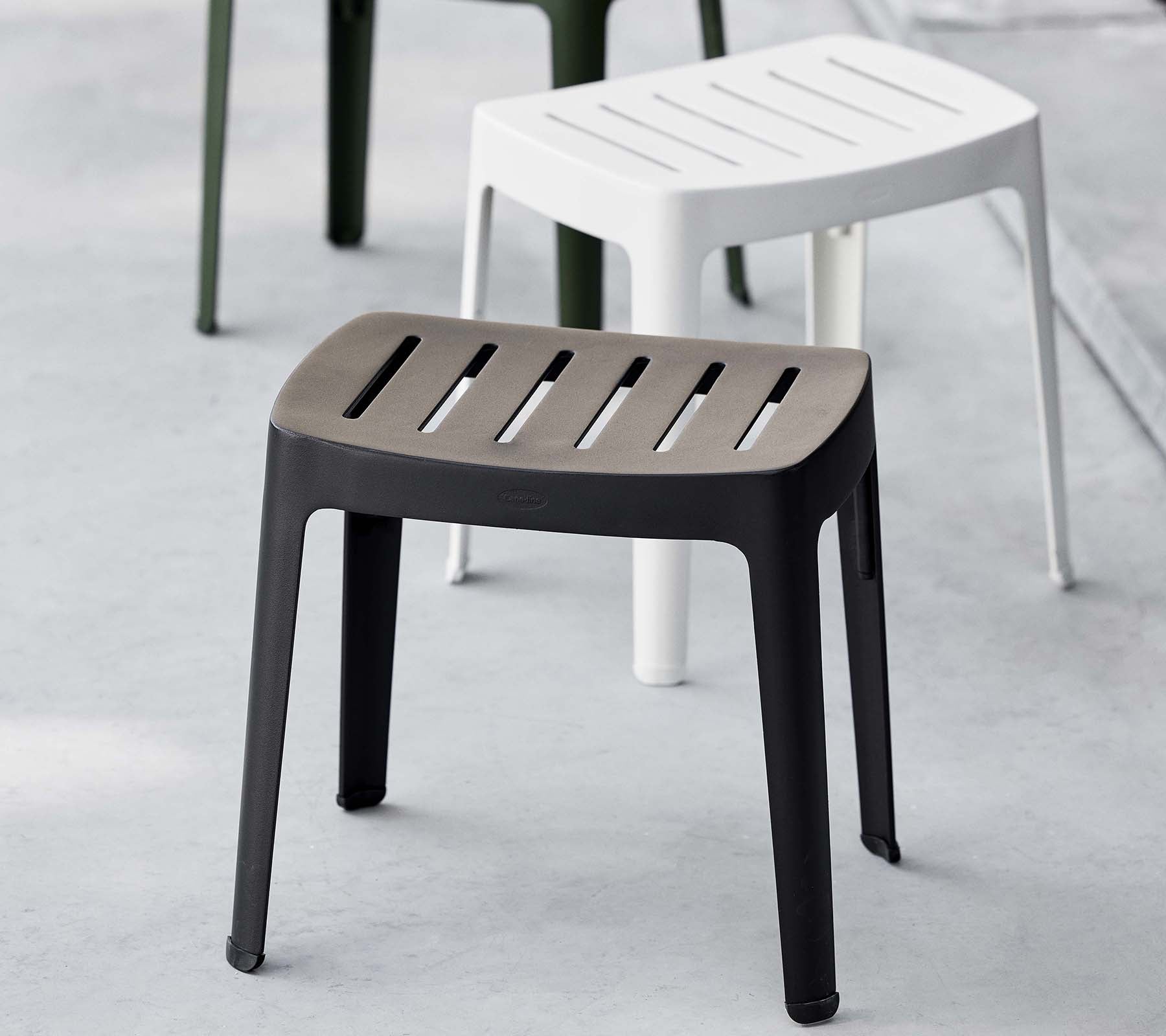 Stylischer Hocker in Schwarz mit lamellenförmiger Oberseite, der ein modernes Design aufweist; ergänzt durch einen weißen Hocker im Hintergrund.