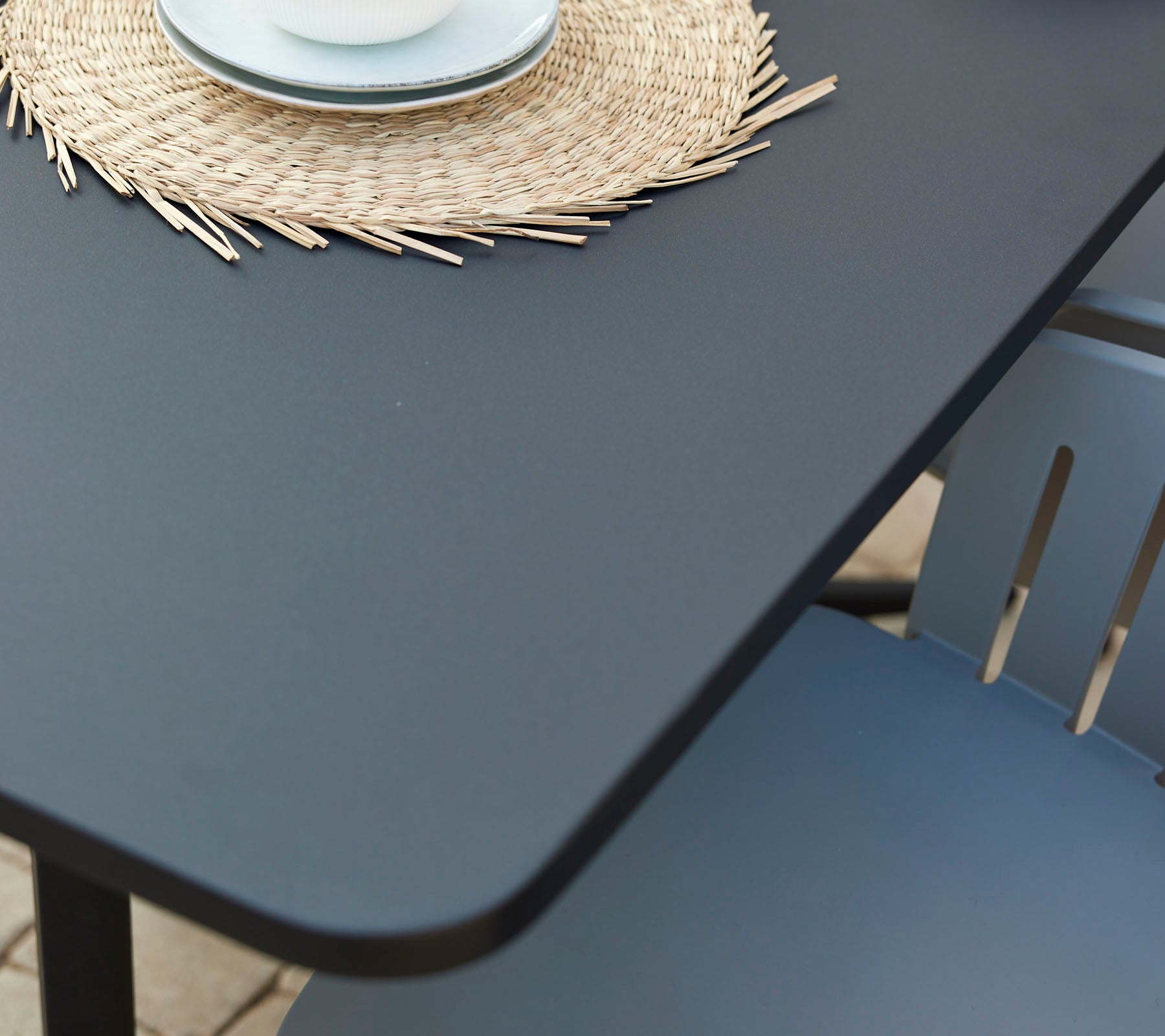 Ein moderner Café-Tisch mit einer glatten Oberfläche, begleitet von einem dekorativen runden Platzdeckchen und einer Tasse auf einem gemütlichen Stuhl.