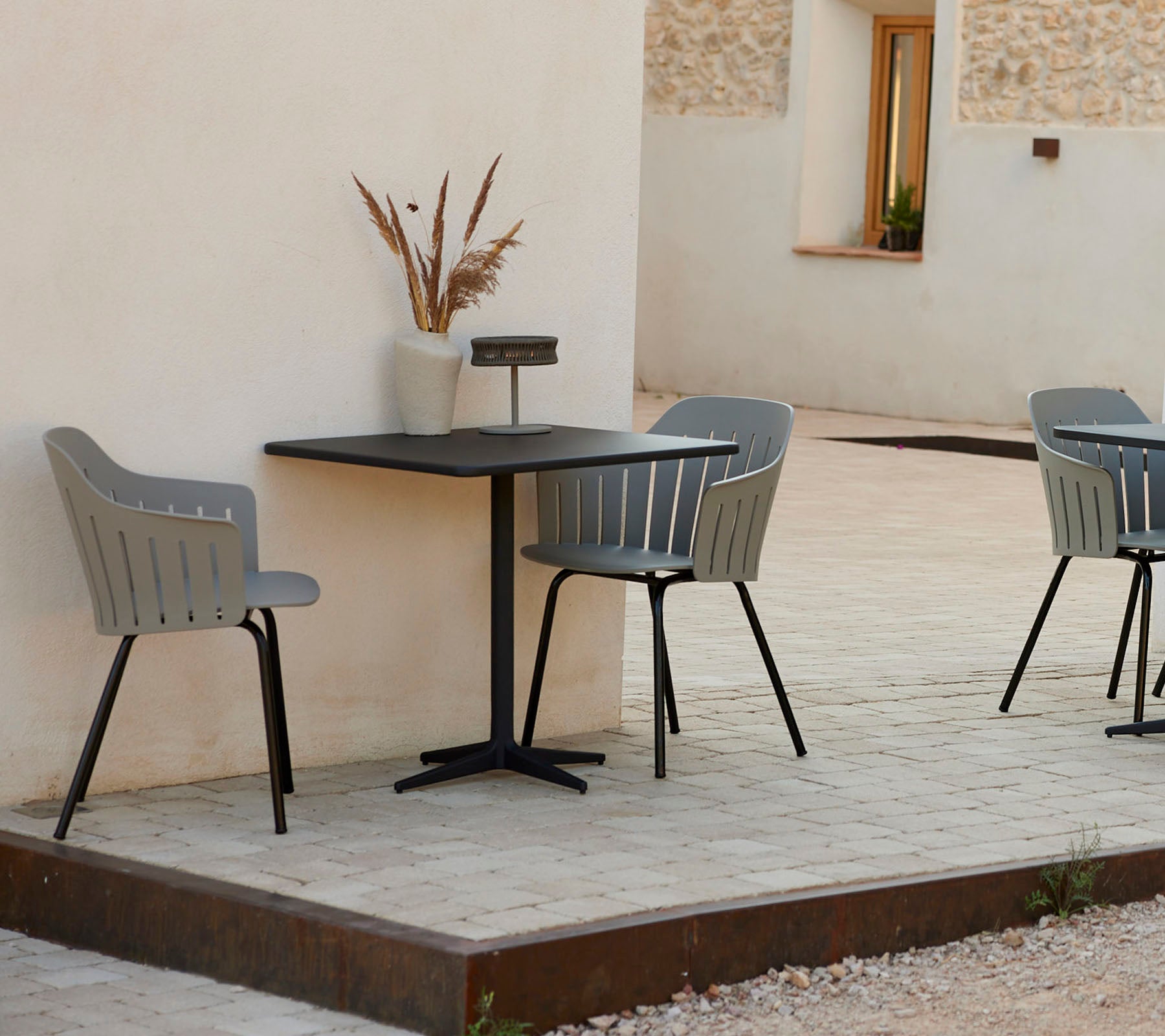 Ein moderner Café-Tisch mit zwei stilvollen grauen Stühlen, begleitet von einer dekorativen Vase, vor einem schlichten Hintergrund.