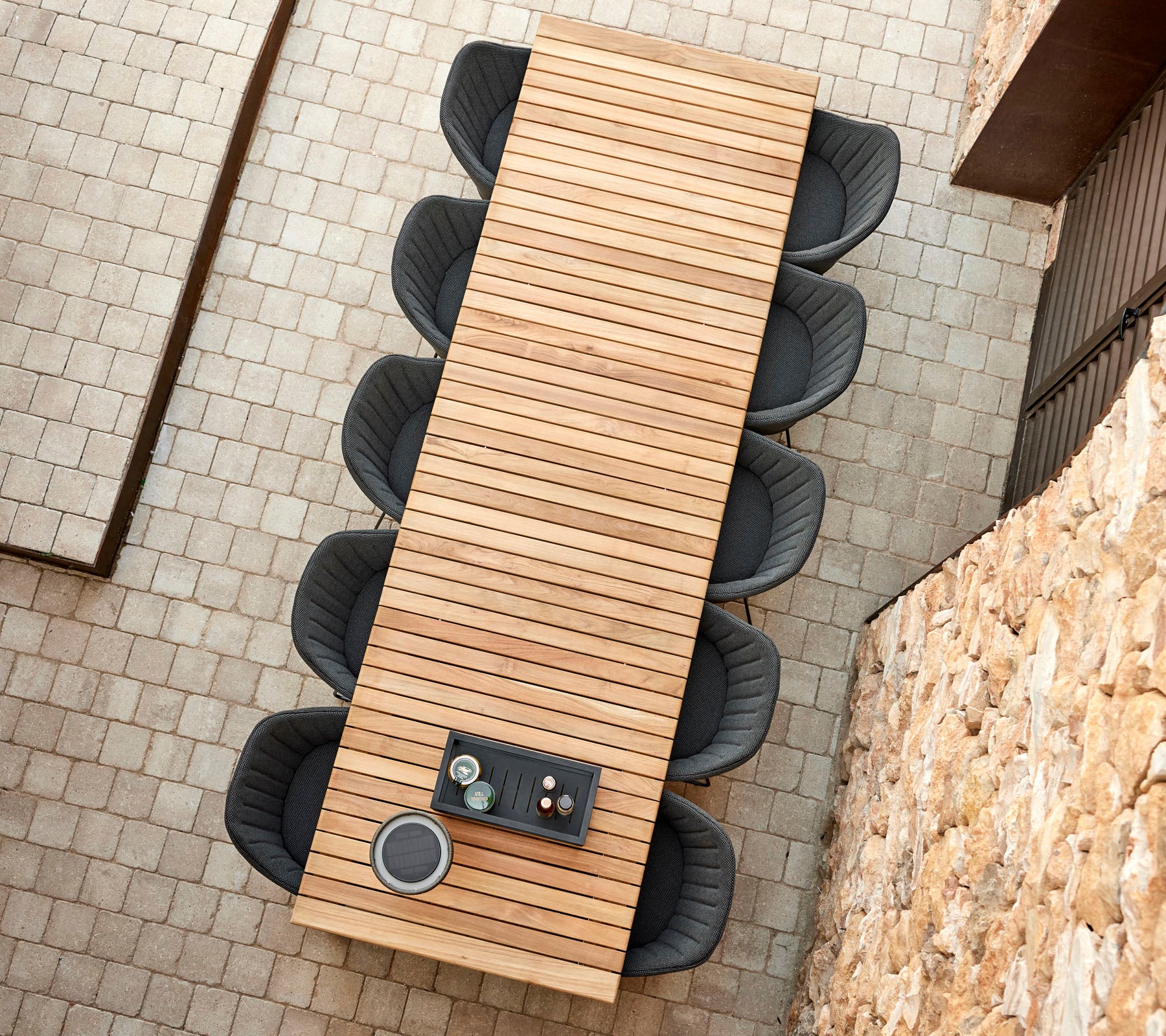 Ein langer Holztisch mit Lamellen-Design, umgeben von runden schwarzen Stühlen, mit einem kleinen Tablett mit Tassen darauf.