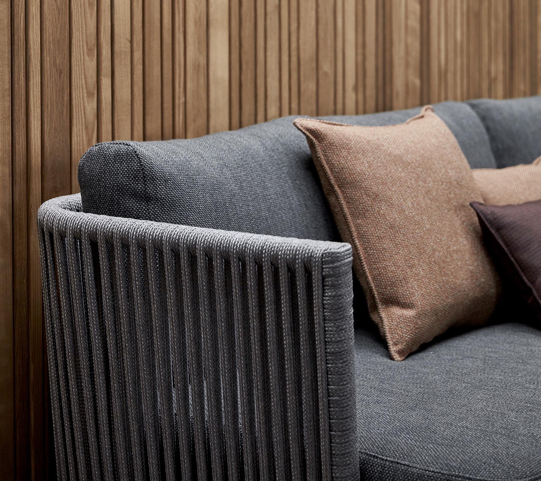 Stylische Sofa mit einem strukturierten grauen Stoff und dekorativen Kissen in Erdtönen sowie einem senkrecht gestreiften Armlehnen-Design.