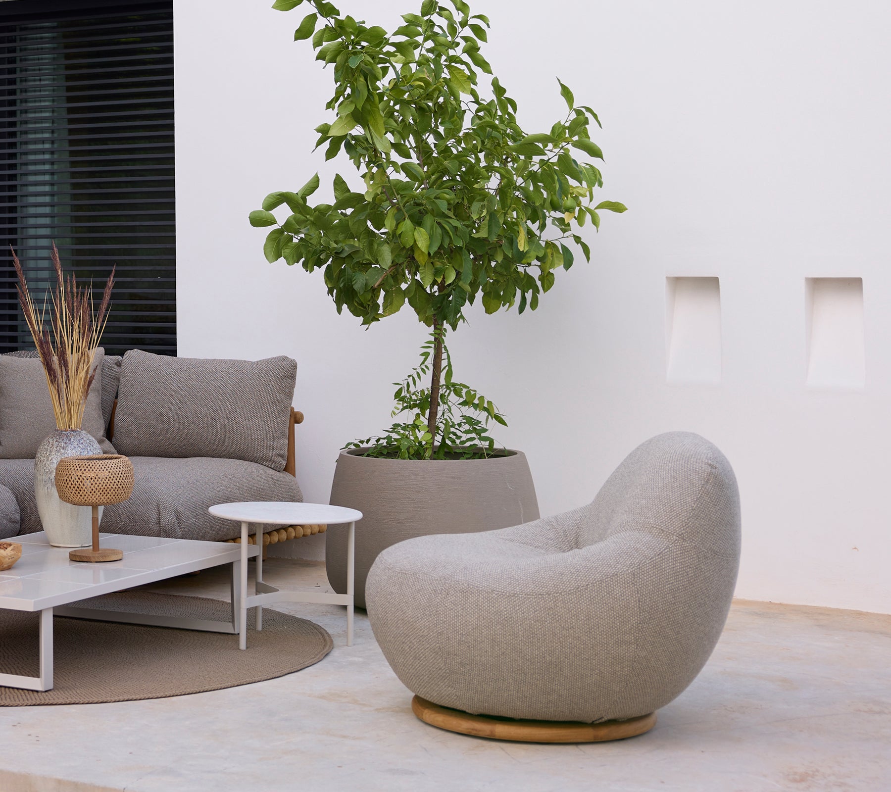 Moderner Loungebereich mit einem grauen Stuhl, Sofa, weißem Couchtisch und grüner Pflanze.