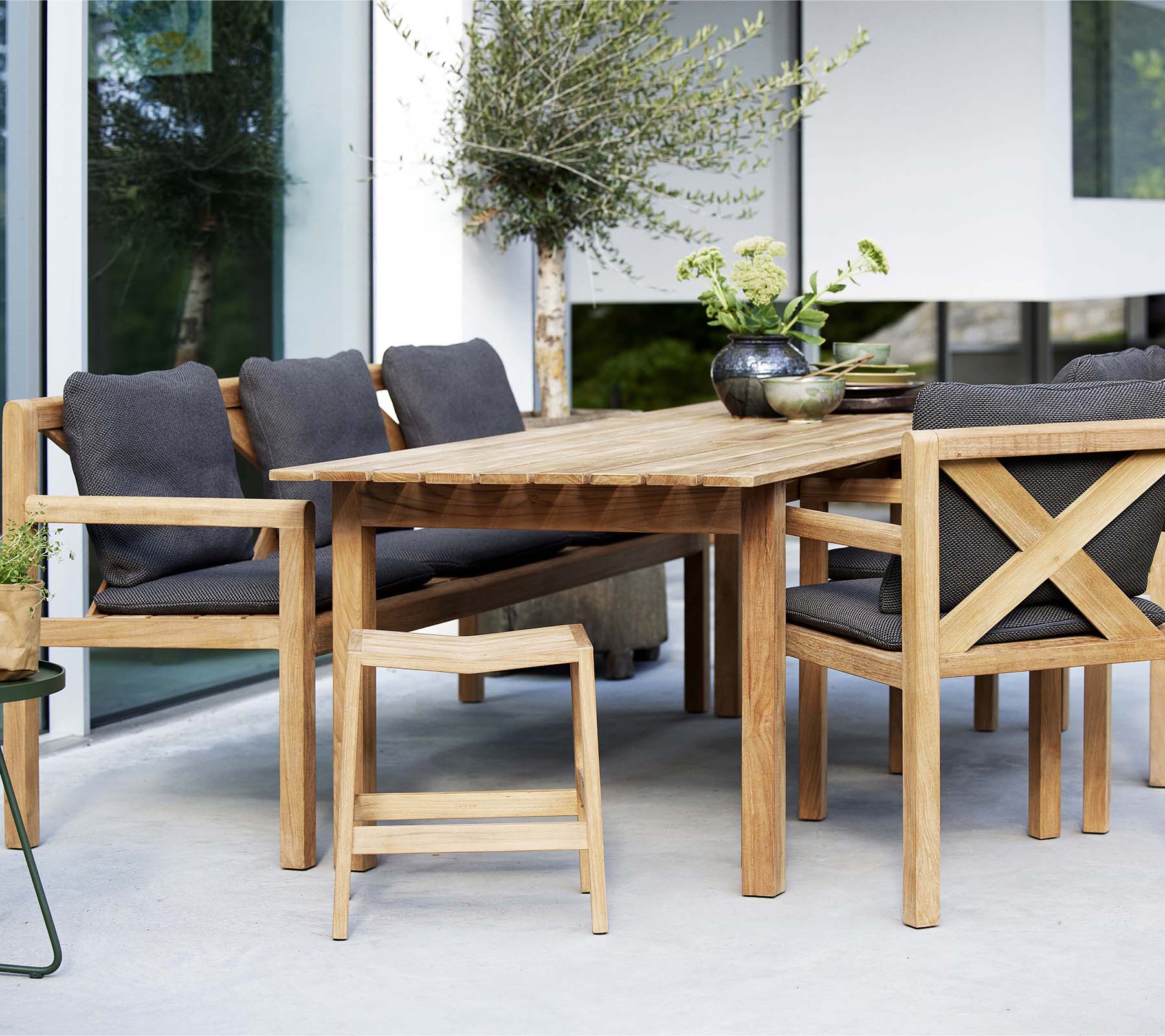 Ein Holztisch umgeben von stilvollen Stühlen und einer Bank, mit weichen Kissen und dekorativen Pflanzen für einen einladenden Sitzbereich.