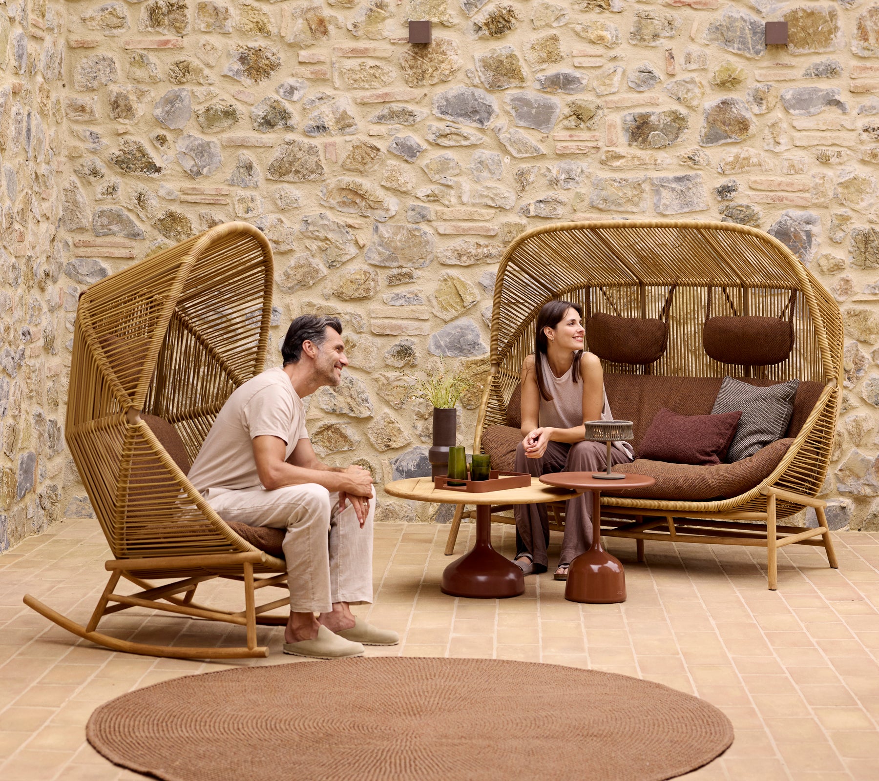 Zwei Personen entspannen sich in stilvollen Hive-Schaukelstühlen und einer Hive-Couch, umgeben von Glaze-Couchtischen und einem weichen Strickteppich.