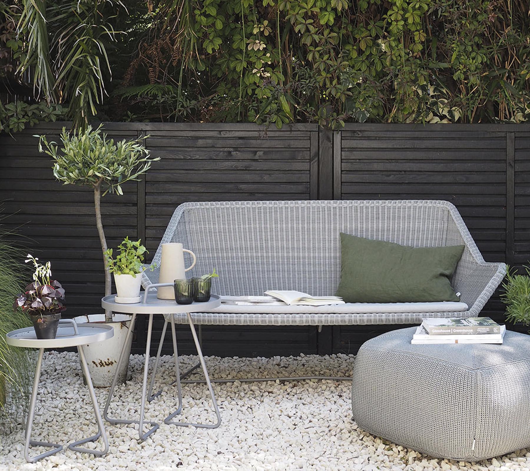 Minimalistische Außenmöbelanordnung mit einem stilvollen Sofa, Beistelltischen und dekorativen Pflanzen auf einer Kiesoberfläche.