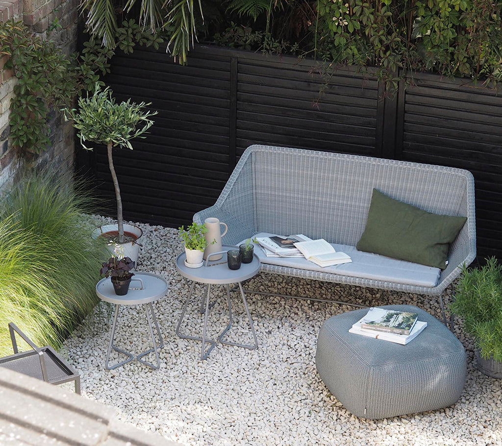 Moderne graue Sofa mit grünem Kissen und grauem Beistelltisch in einem minimalistischen Loungebereich.