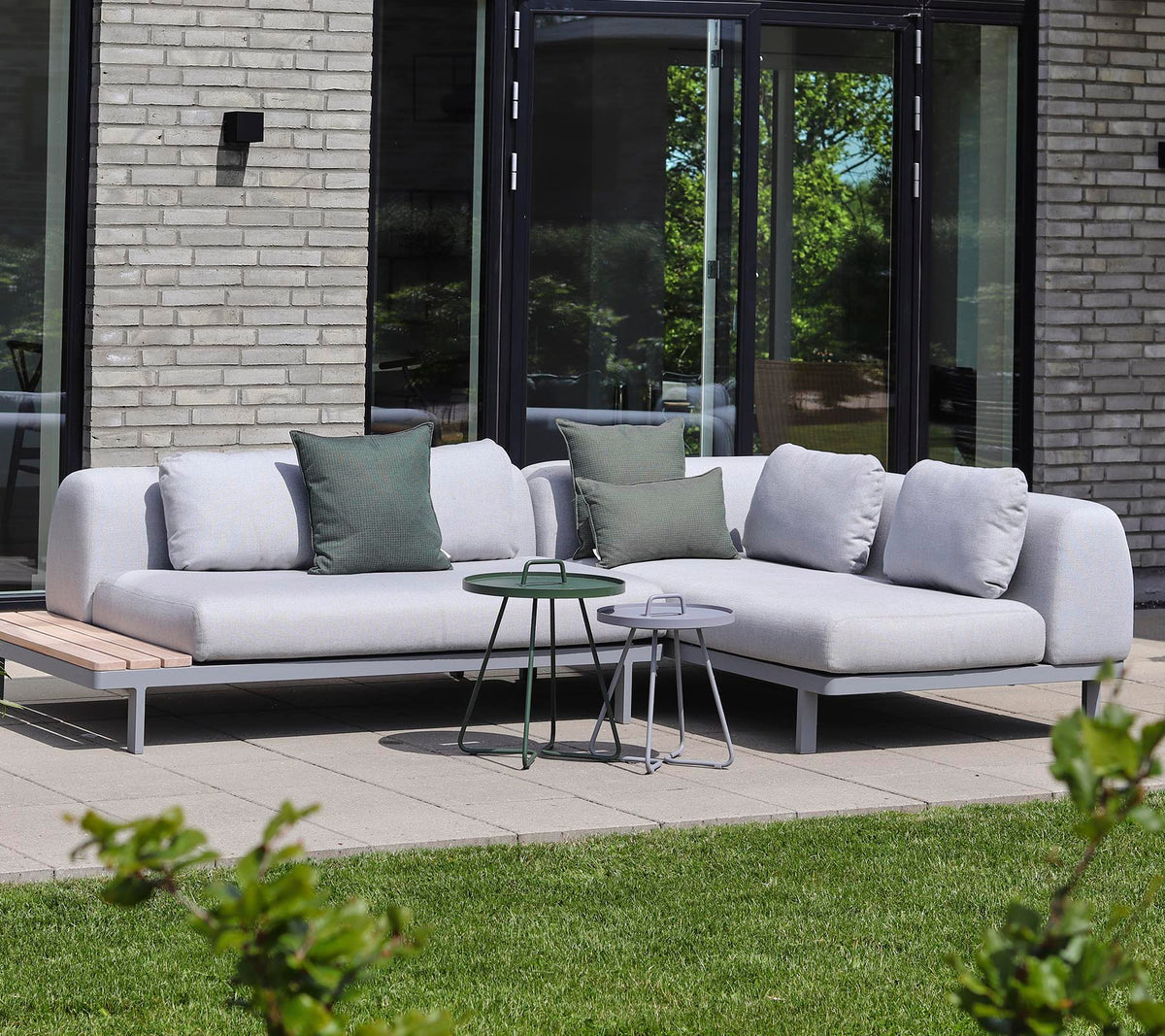 Modernes Ecksofa aus hellem Stoff mit dekorativen Kissen, kombiniert mit kleinen Beistelltischen in einer ruhigen Umgebung.