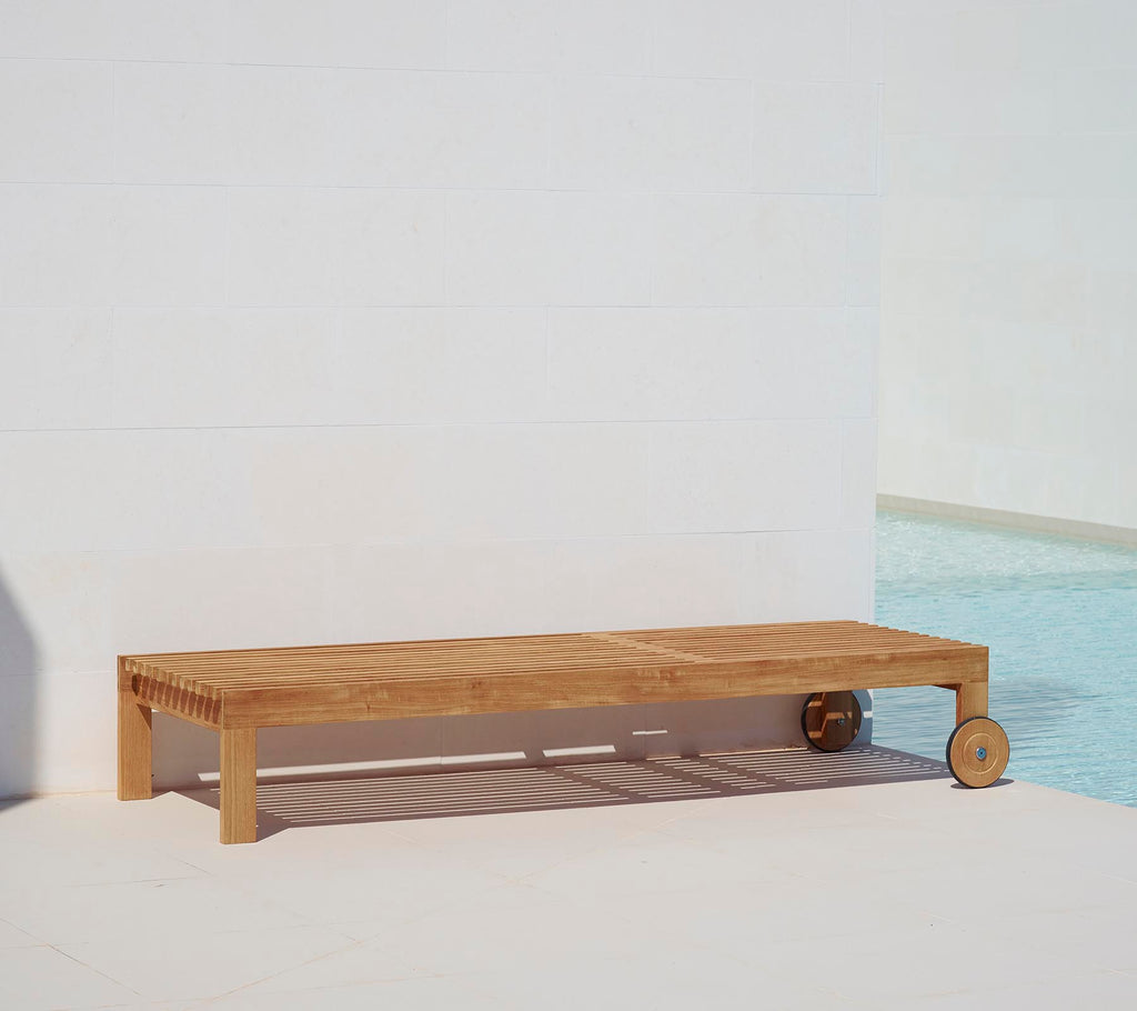 Holzliege mit minimalistischer Gestaltung, ausgestattet mit einer glatten Oberfläche und einem Rad für einfache Mobilität. Ideal zum Entspannen am Pool.