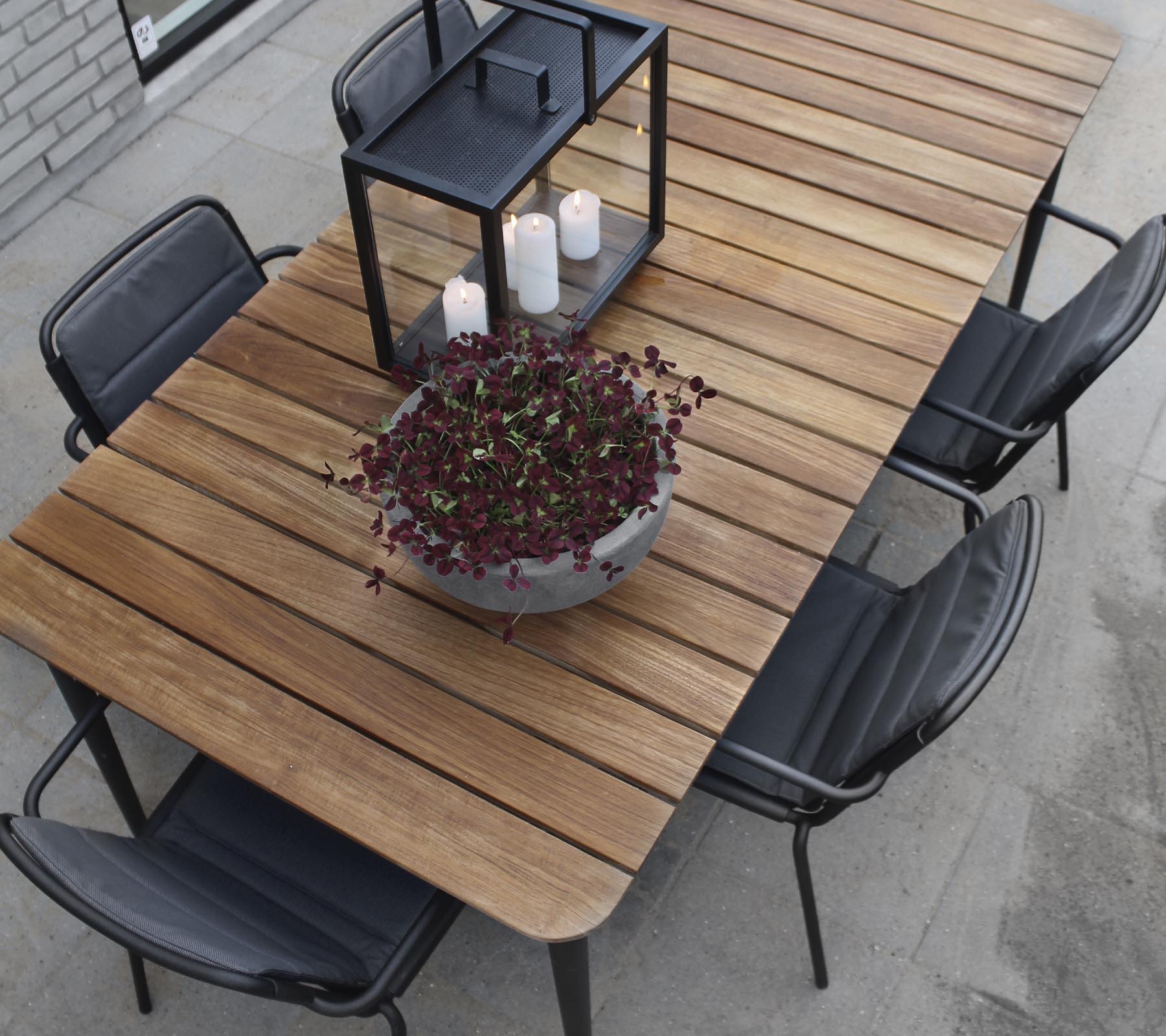Ein Holztisch mit schwarzen Stühlen, mit einem großen Blumenkübel und einem Kerzenleuchter als Mittelpunkt.