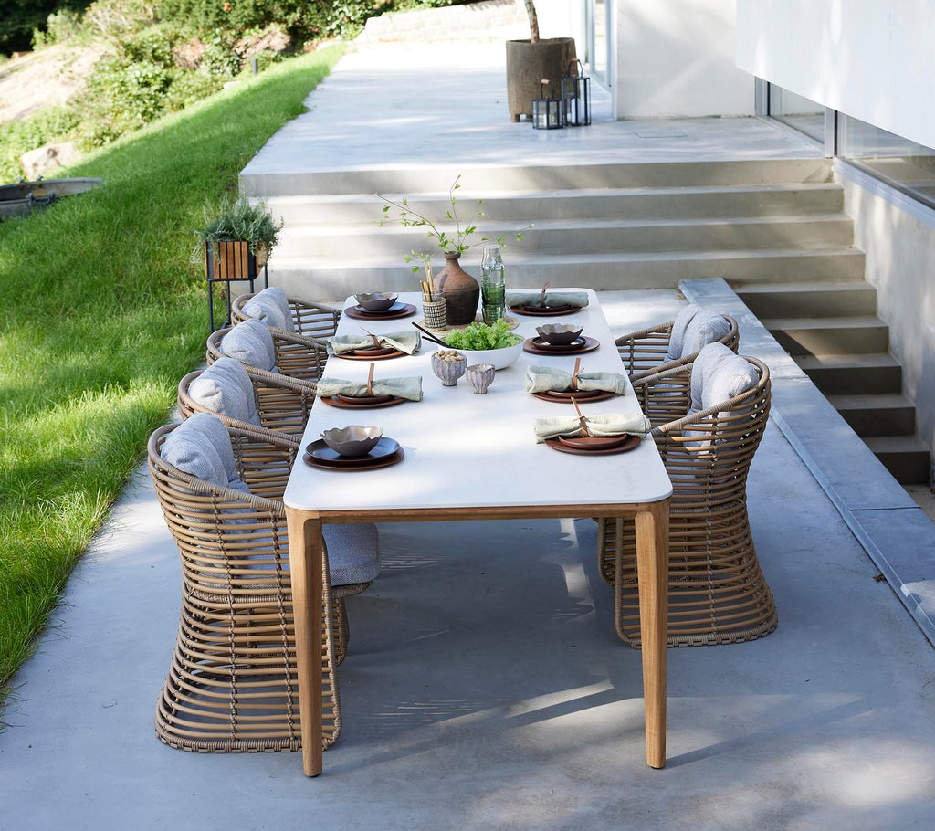 Ein stilvolles Esszimmer-Set für den Außenbereich mit runden Korbstühlen, elegant angerichtet mit Tellern und einem Mittelpunkt aus Grünpflanzen.
