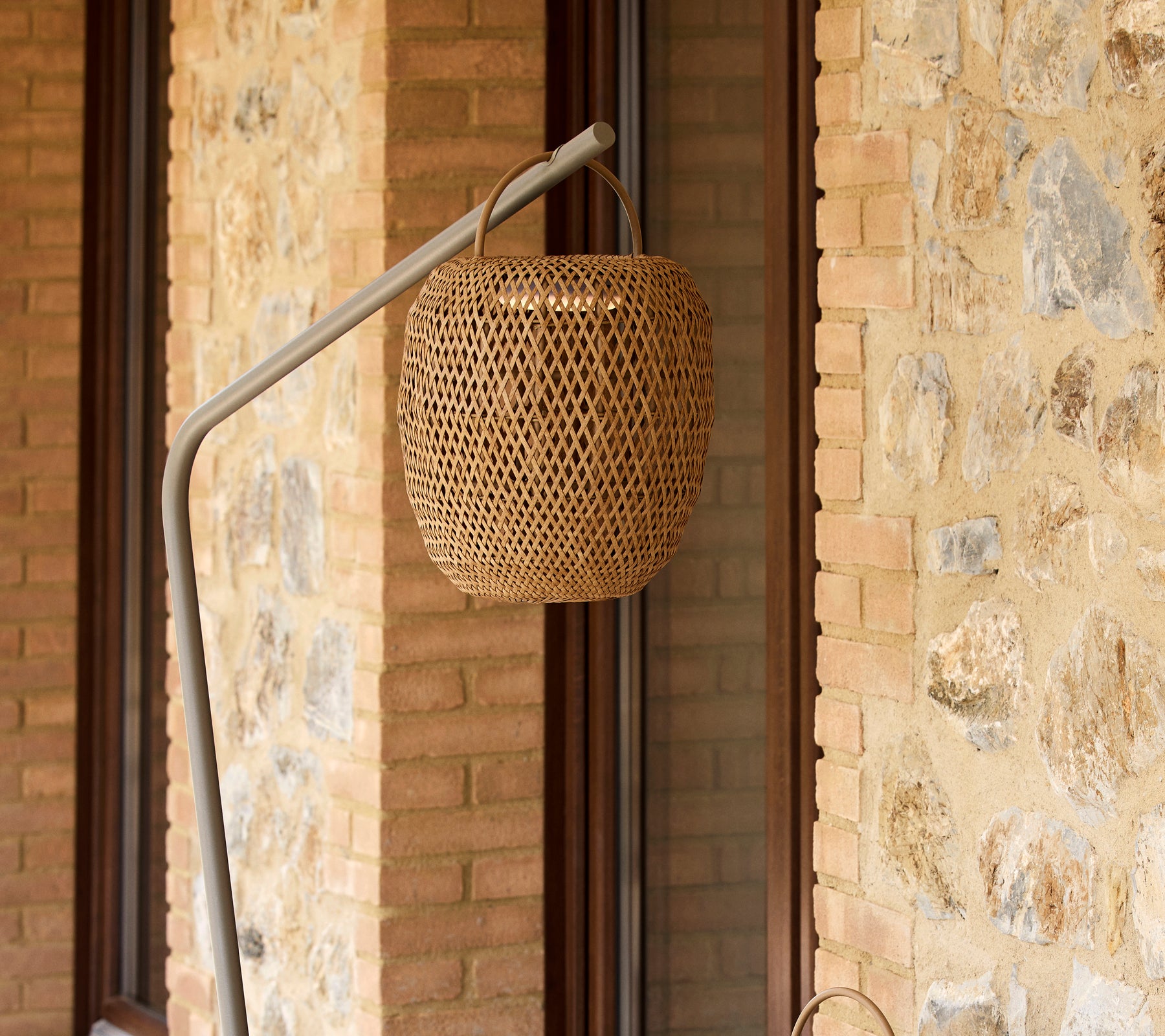 Eine gewebte leuchtende Lampe, die an einem schlanken Ständer hängt und eine strukturierte Steinwand ergänzt.