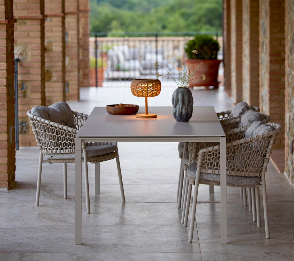 Eine kleine, leuchtende Tischlampe auf einem eleganten Tisch, umgeben von stilvollen Gartenstühlen, die eine gemütliche und einladende Atmosphäre schaffen.