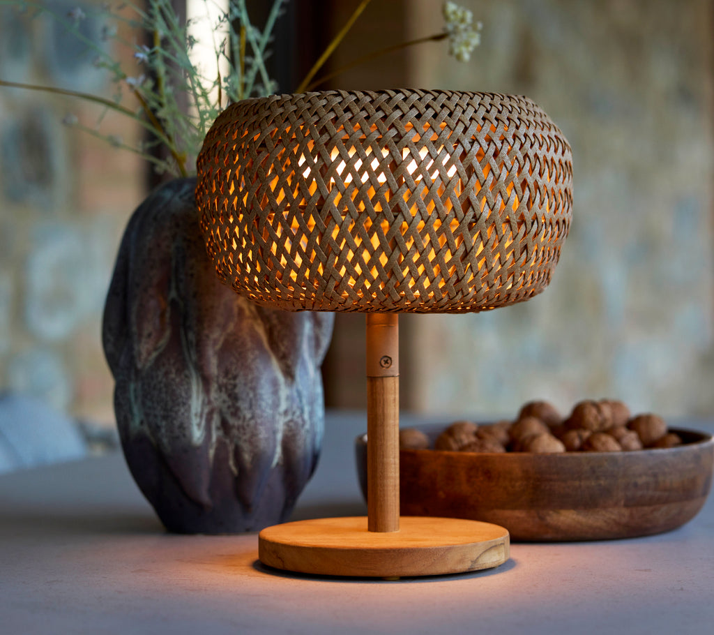 Kleine gewebte Lampe mit warmem Licht, ergänzt durch eine dekorative Vase und eine Schüssel mit Nüssen, die eine gemütliche Atmosphäre schaffen.