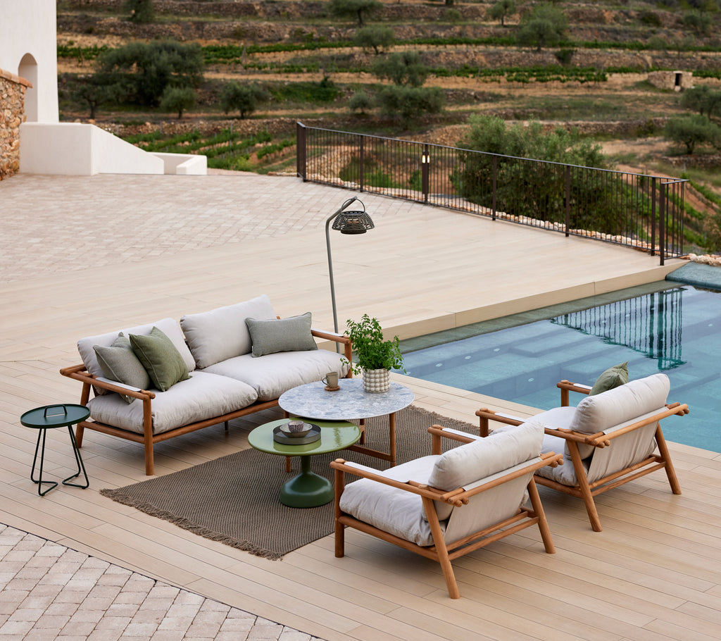 Gemütlicher Loungebereich mit einem gestrickten Teppich, stylischen Sitzmöglichkeiten, einem kleinen Tisch und einer Stehlampe in der Nähe eines Pools mit malerischer Aussicht.
