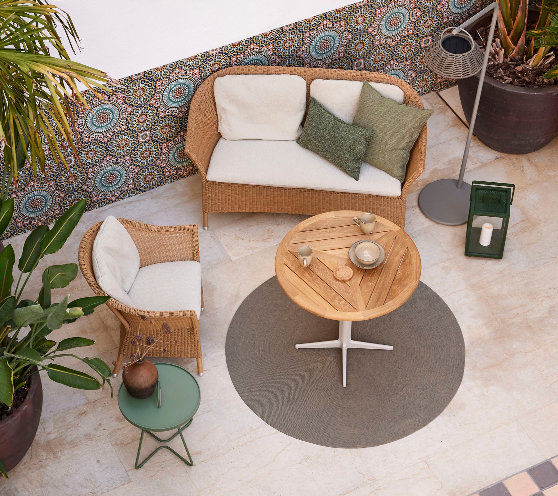 Eine gemütliche Sitzgelegenheit mit einem Rattansofa, einem runden Holztisch und Topfpflanzen, die eine stilvolle Atmosphäre schaffen.