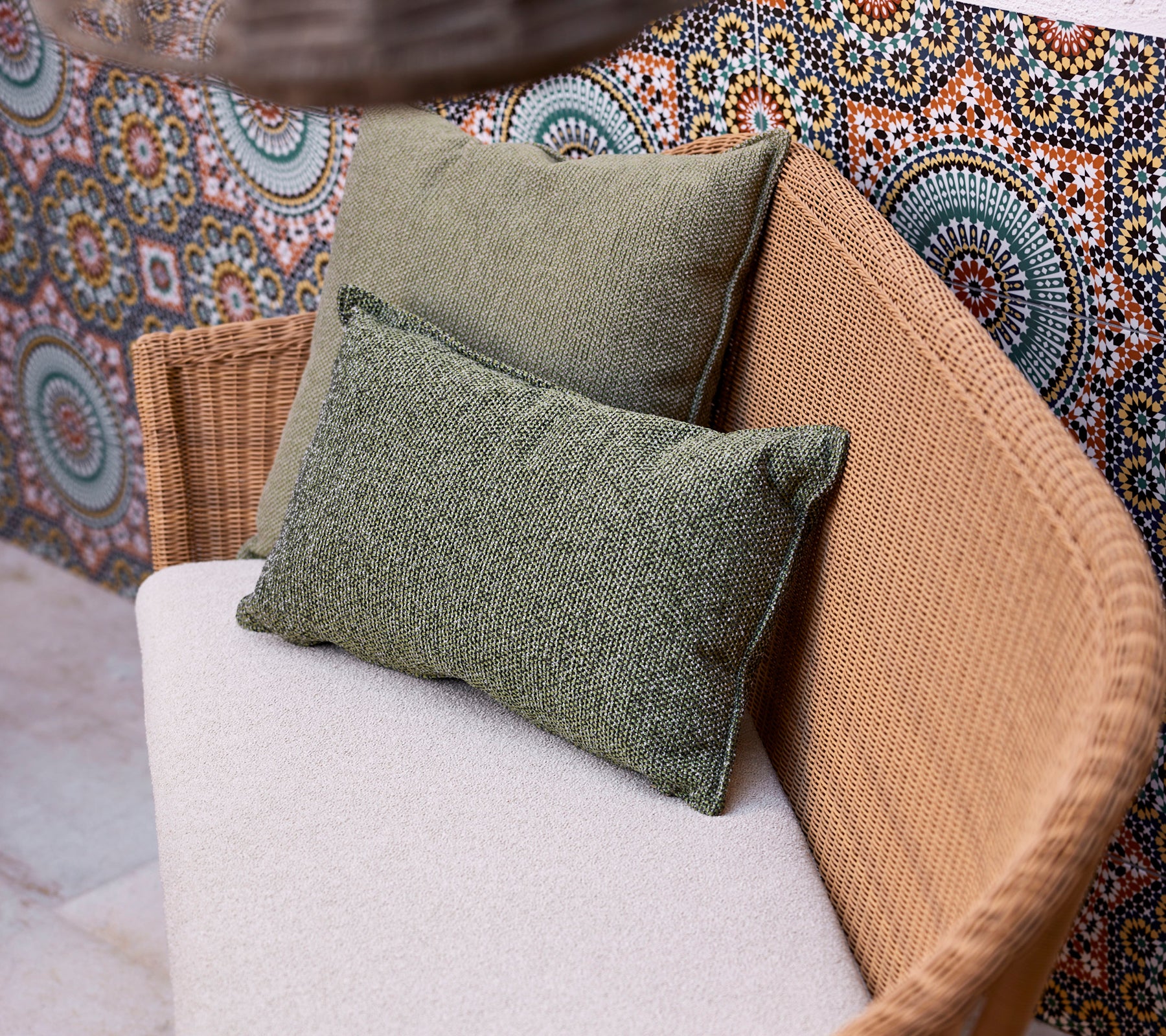 Zwei grüne Scatterkissen auf einem hellen Sofa, platziert vor einem lebhaften, gemusterten Hintergrund mit kreisförmigen Designs.