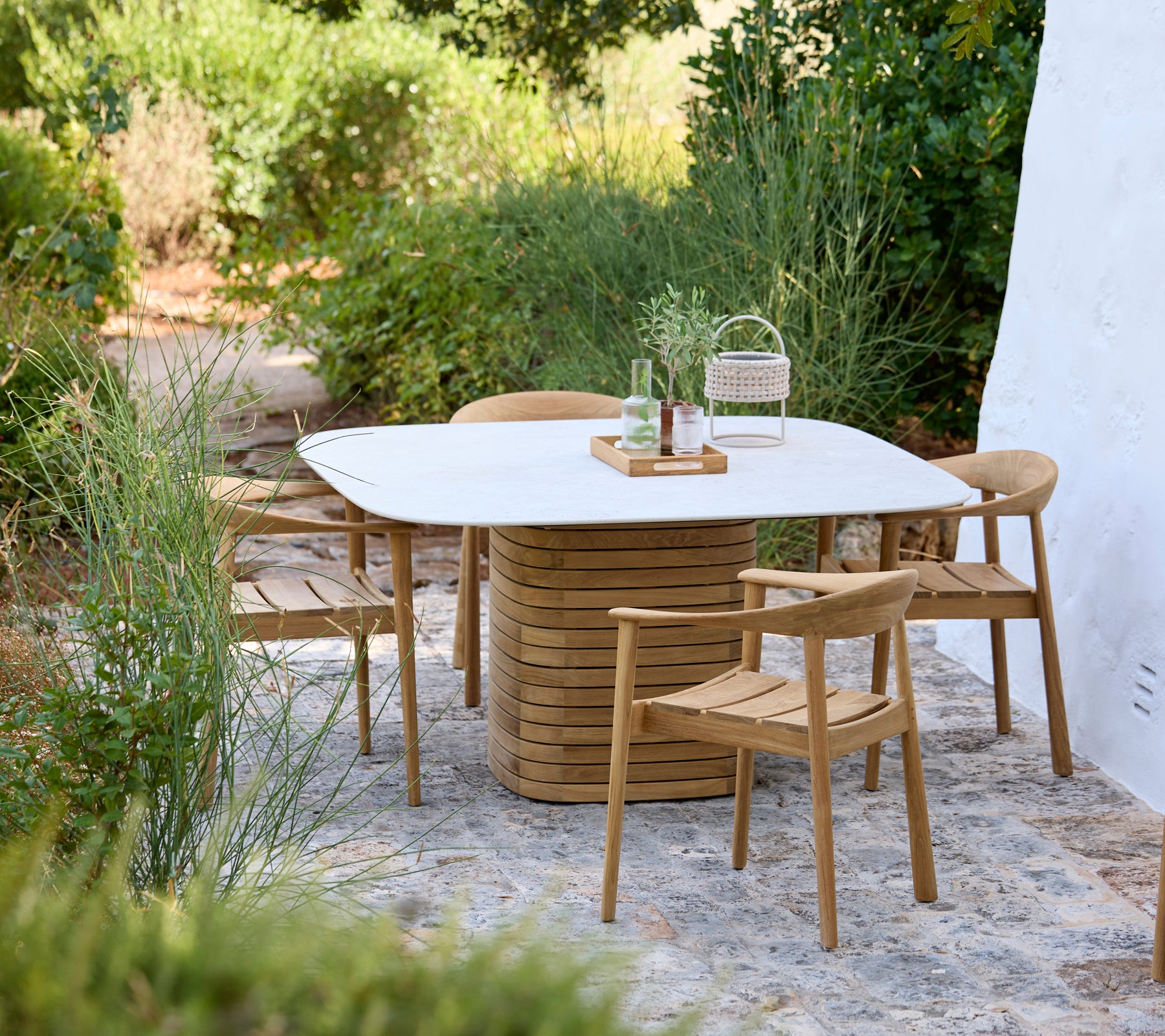Moderne Außenbereich mit einem weißen Tisch und Holzstühlen, umgeben von Grün.