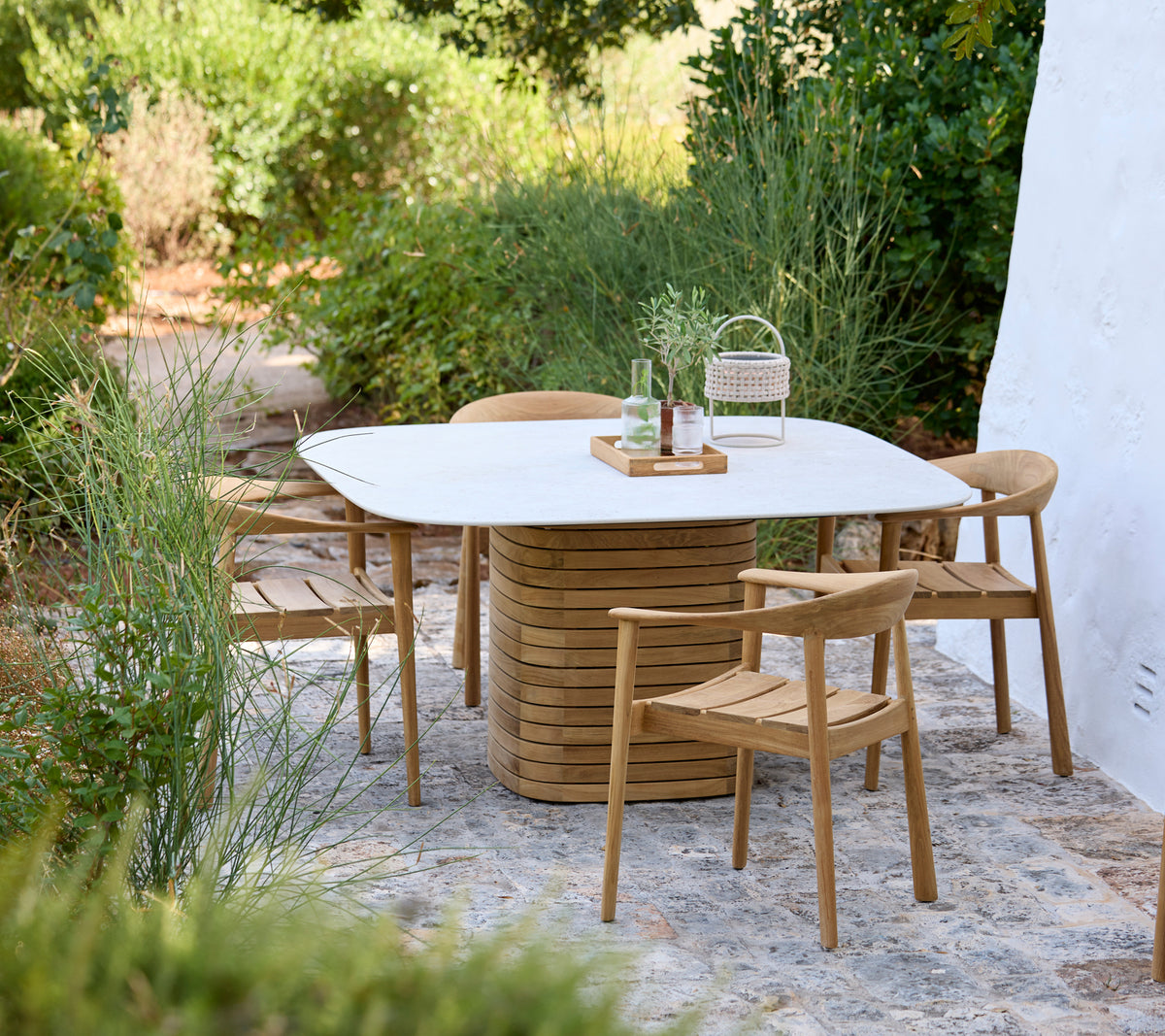 Moderne Außenbereich mit einem weißen Tisch und Holzstühlen, umgeben von Grün.