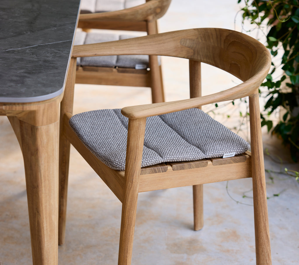 Moderne Holzstuhl mit grauem Kissen neben einem Tisch in einer Lounge-Umgebung.