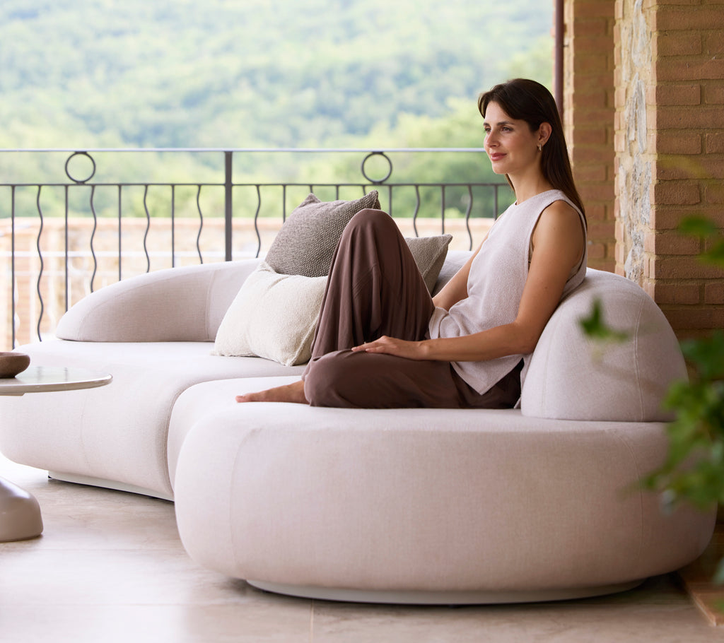 Eine Frau sitzt bequem auf einem eleganten, modernen Sofa, begleitet von dekorativen Kissen, und genießt eine ruhige Aussicht auf die Natur.