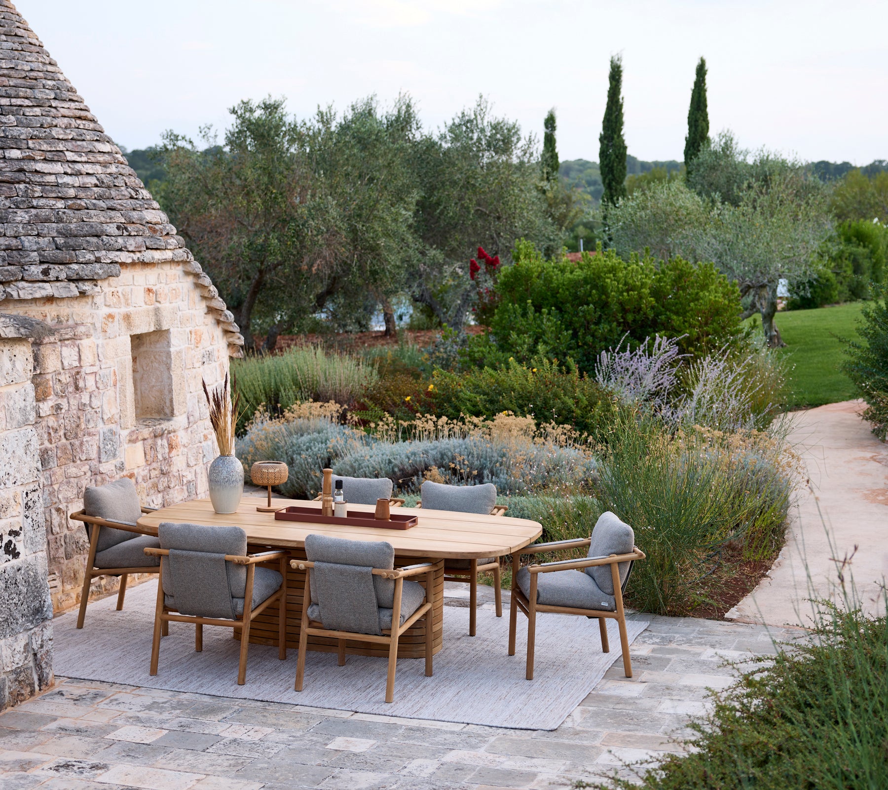 Moderne Außenbereich mit einem runden Tisch und grauen Stühlen, umgeben von Grünpflanzen.