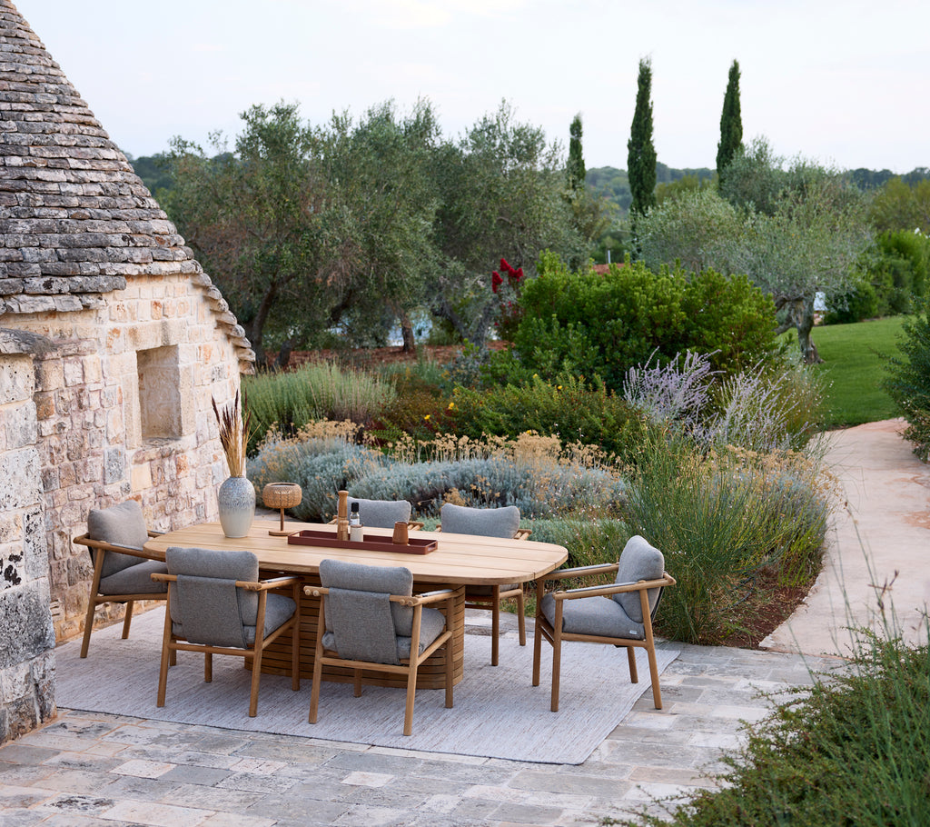 Moderne Außenbereich mit einem runden Tisch und grauen Stühlen, umgeben von Grünpflanzen.