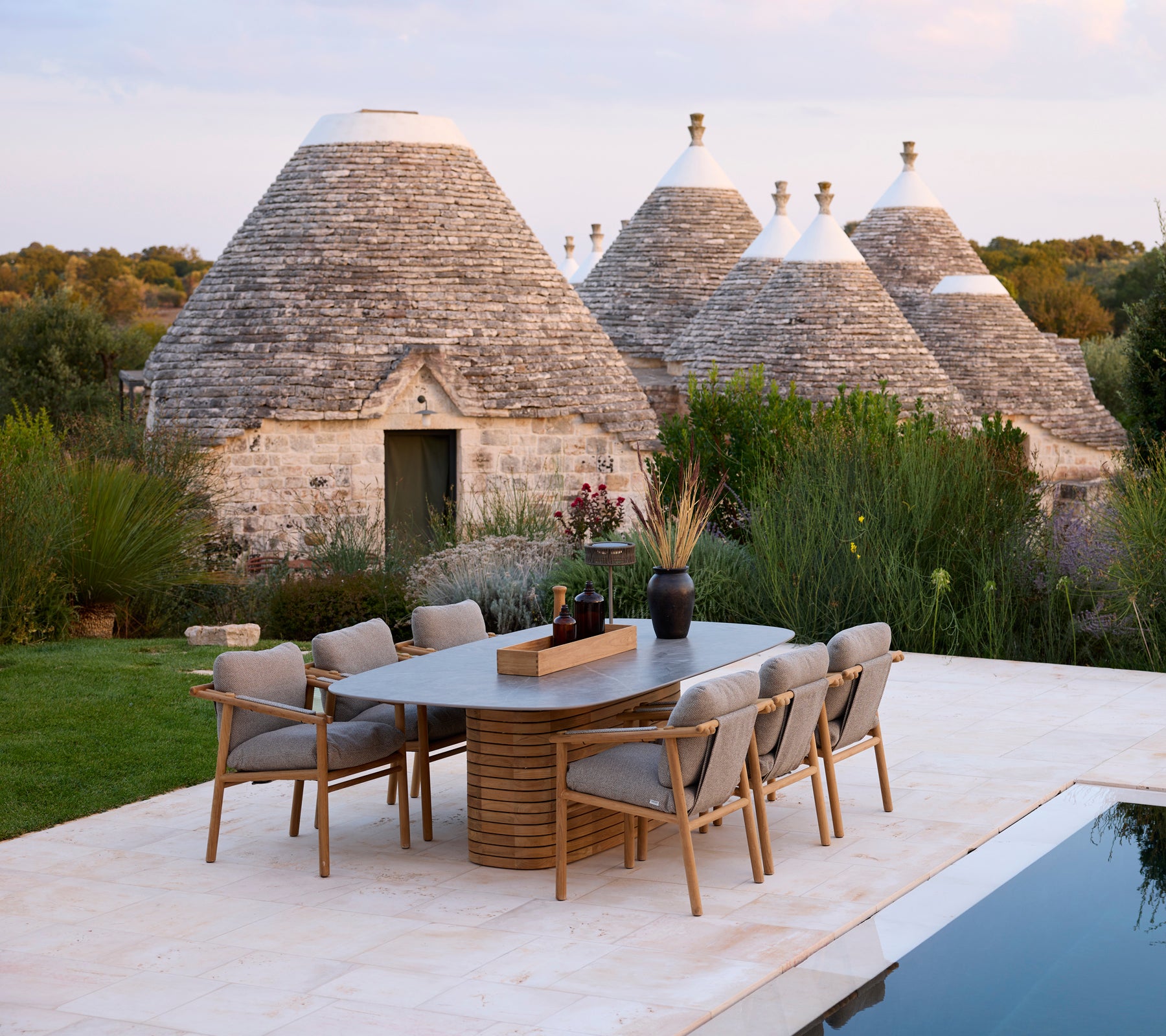 Graue Esszimmerstühle um einen rechteckigen Tisch in der Nähe traditioneller Trullo-Strukturen.