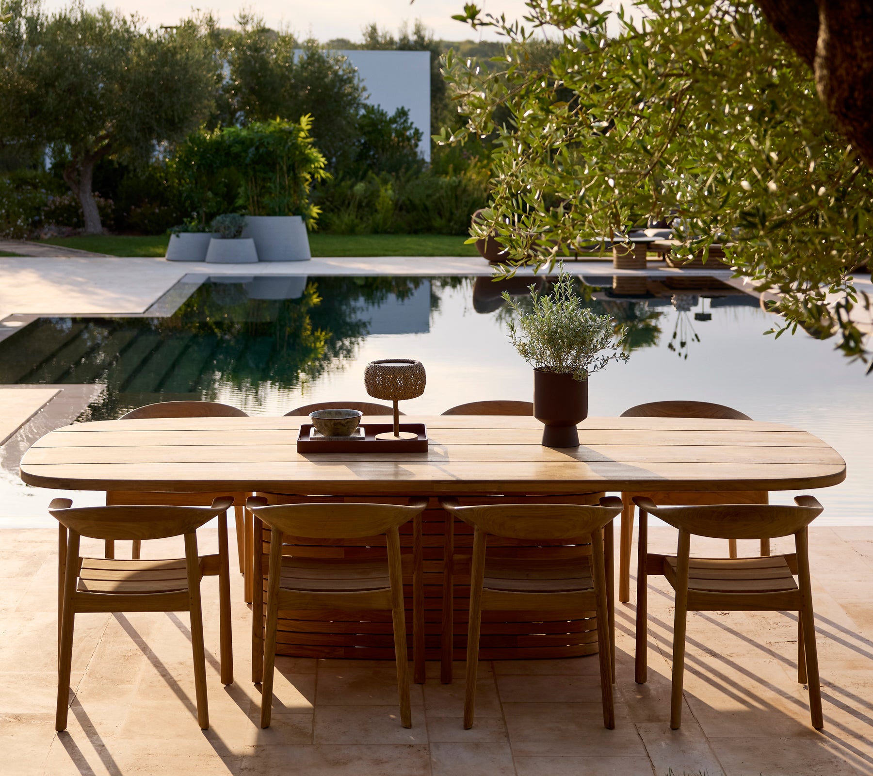 Modernes Holz-Esszimmertisch- und Stuhlset neben einem Pool, umgeben von Grünflächen.