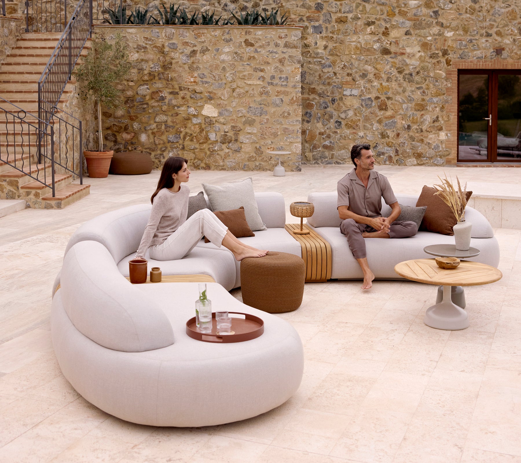 Eine moderne Lounge-Einrichtung mit einem geschwungenen Sofa, einem runden Hocker und einem stilvollen Couchtisch mit einem Clubtablett, das eine gemütliche Atmosphäre schafft.