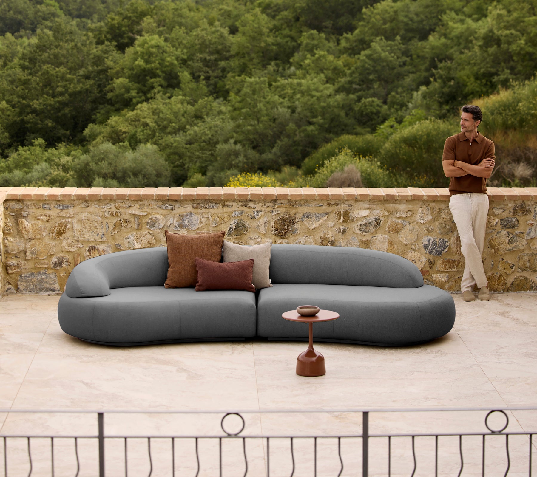 Mellow Lounge-Sofa mit Kissen neben einem eleganten Glaze-Couchtisch, vor einem natürlichen Hintergrund.