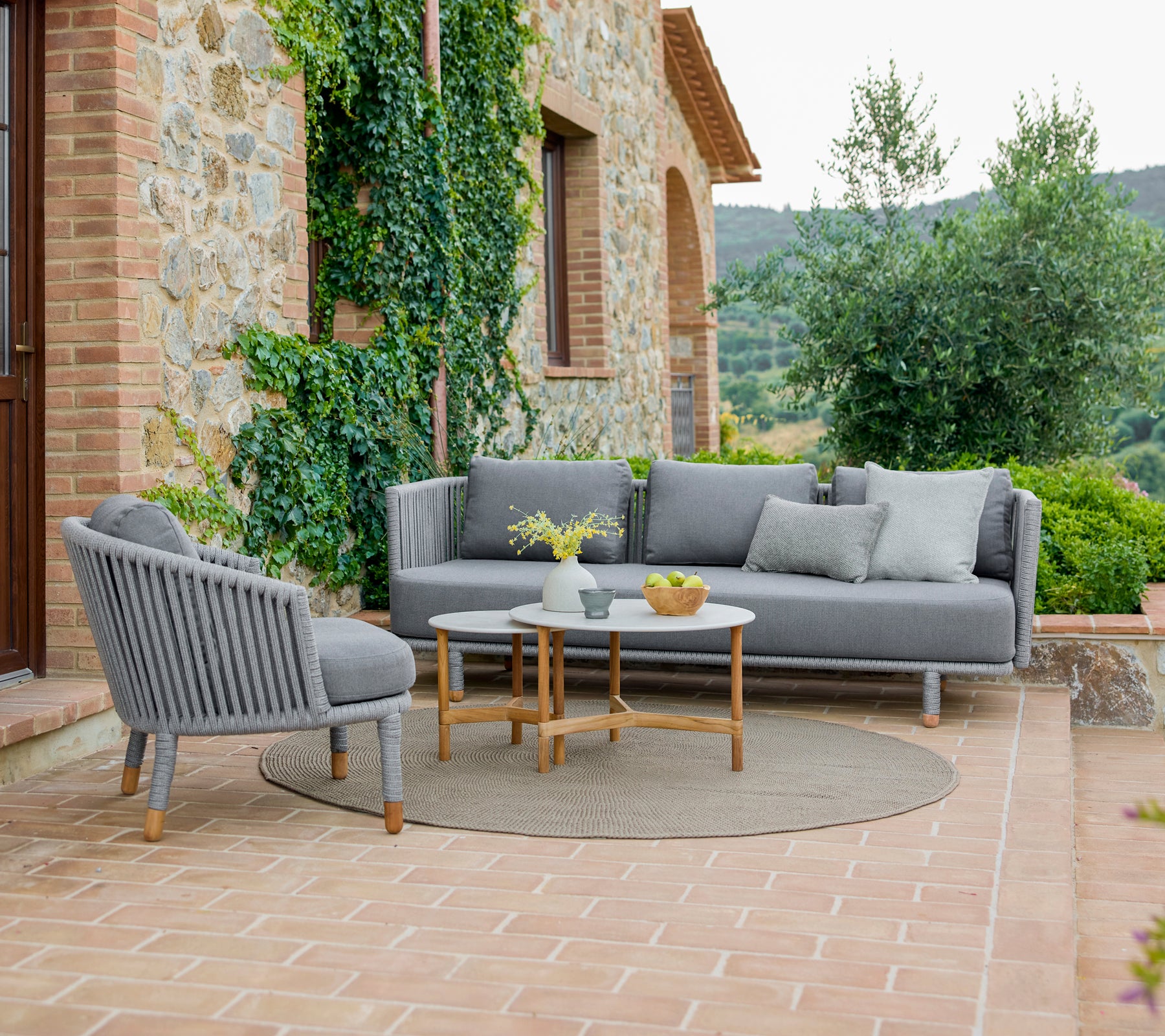 Stilvoller Loungestuhl und Sofa mit einer gemütlichen Anordnung, begleitet von eleganten Couchtischen, umgeben von Grün.