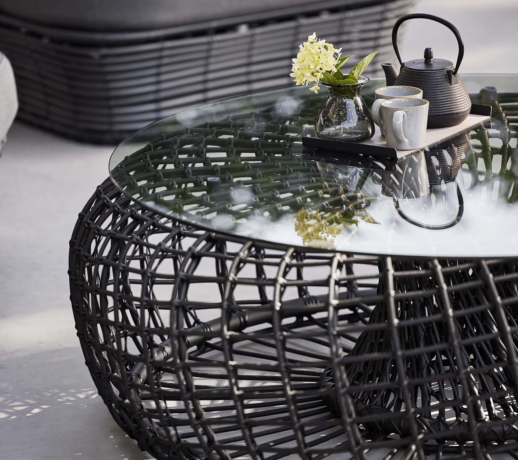 Nest-Kaffe Tisch mit einem geflochtenen Gestell, einer Glasplatte und einem Teeset mit Blumen für einen stilvollen, modernen Look.