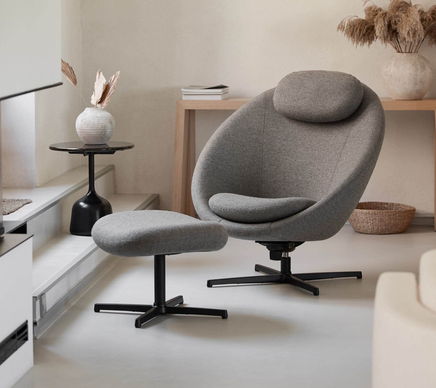 Stylischer grauer Stuhl mit passendem Hocker, der ein elegantes Design und bequeme Kurven aufweist, ergänzt durch moderne Dekorationselemente.