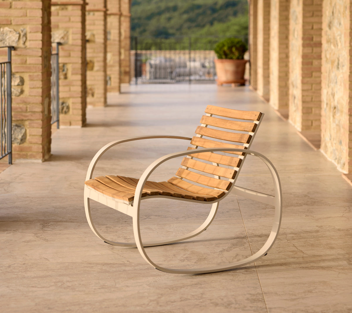 Parc Schaukelstuhl mit einem Aluminiumrahmen und Holzlatten, platziert auf einer Terrasse mit Steinboden und malerischer Kulisse.