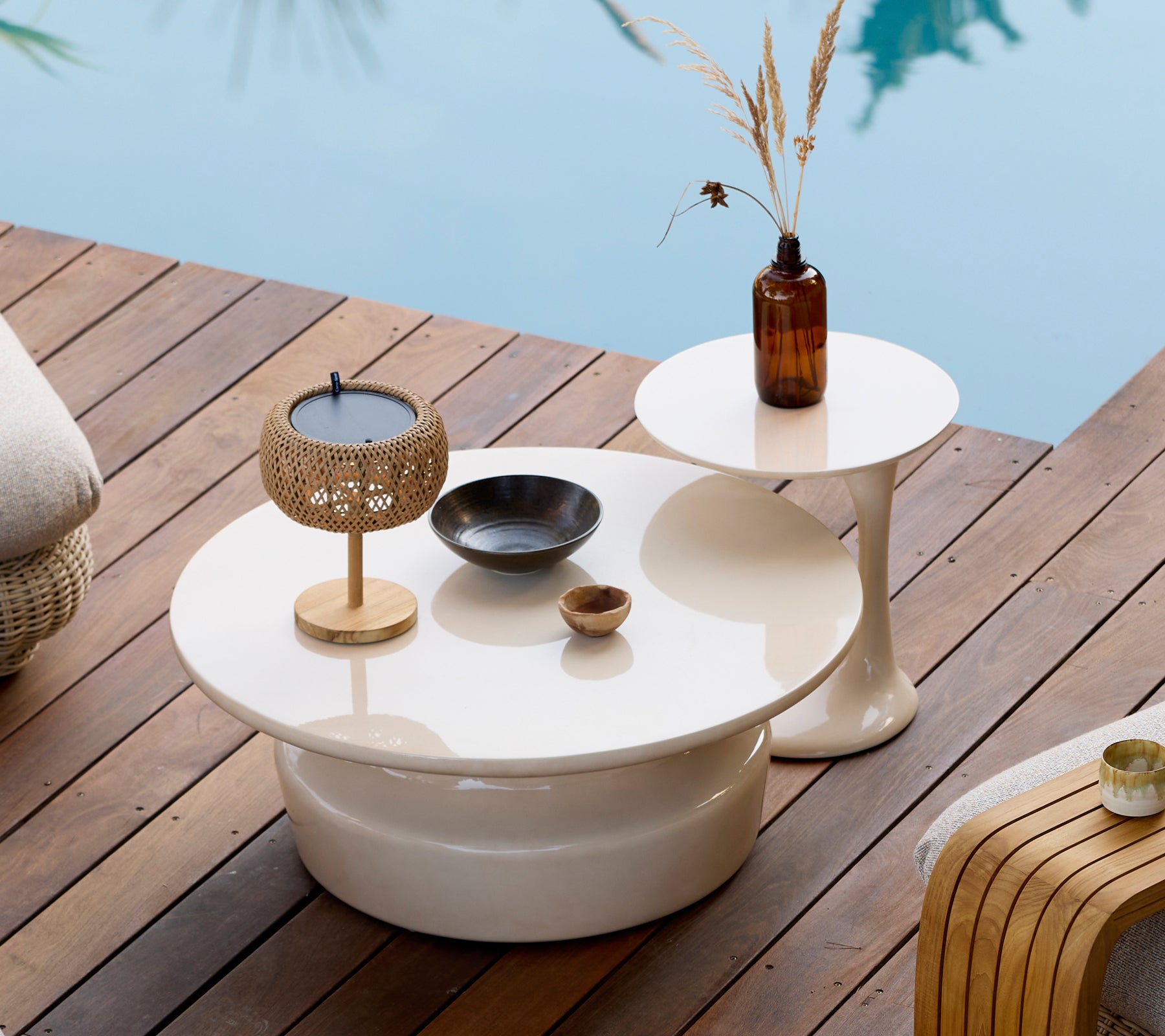 Moderne Außeneinrichtung mit weißen Kaffeetischen und Beistelltischen, goldenen Kerzenhaltern und einer braunen Vase.