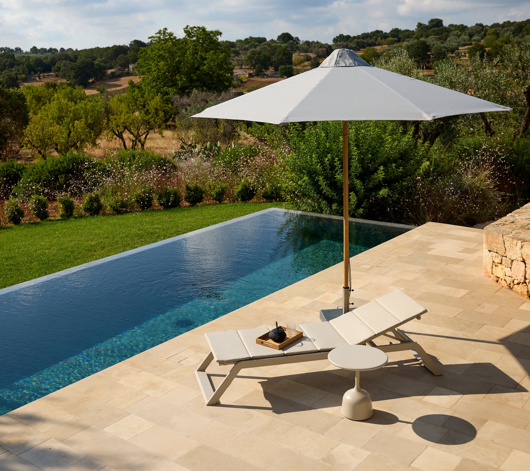 Moderne Außenlounge-Bereich mit einem weißen Stuhl, Sonnenschirm und Beistelltisch neben einem Pool.