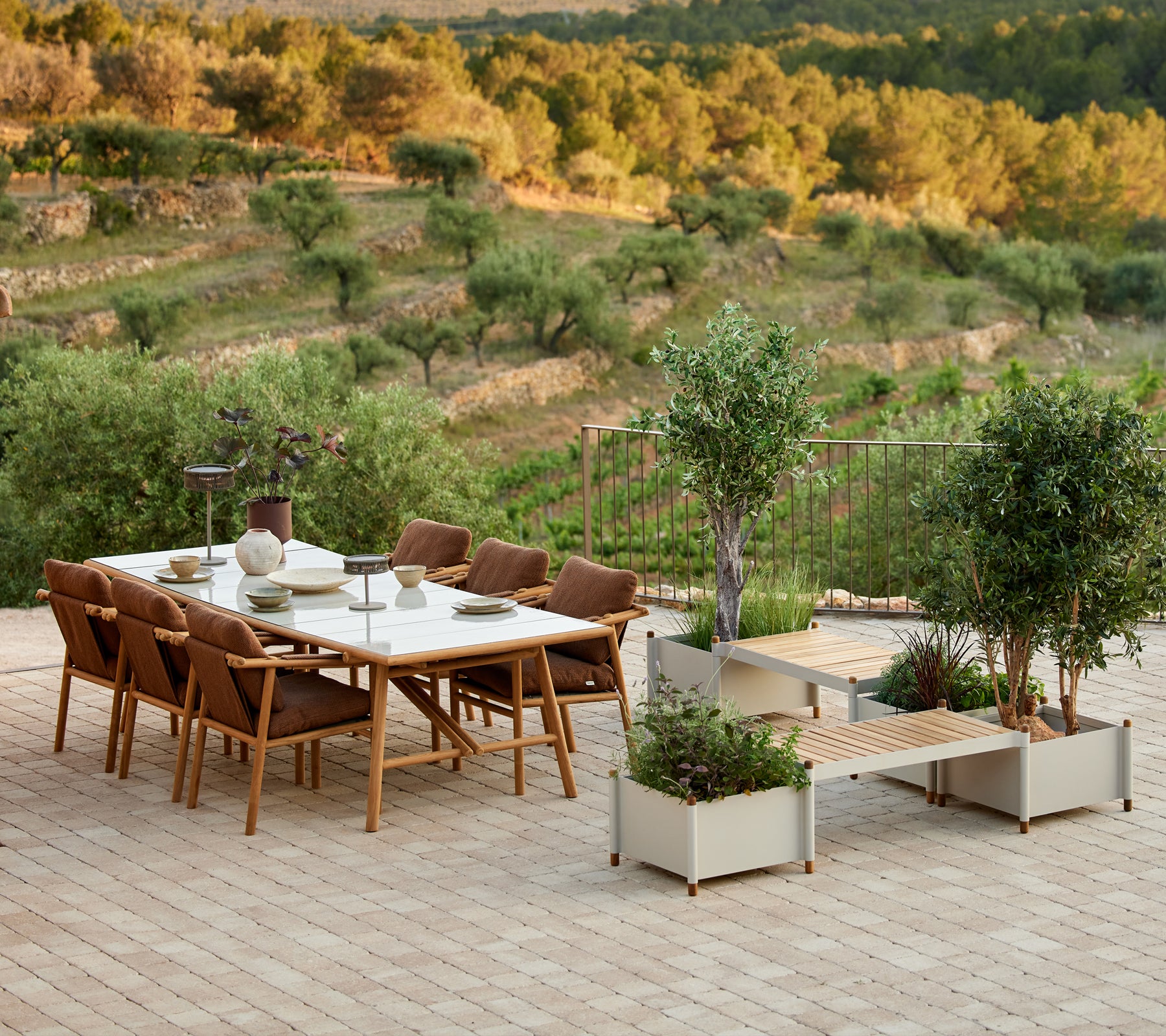 Stylisches Teakholz-Esszimmer-Set mit Stühlen und einer Pflanzenbank, umgeben von Grün und malerischer Landschaft.