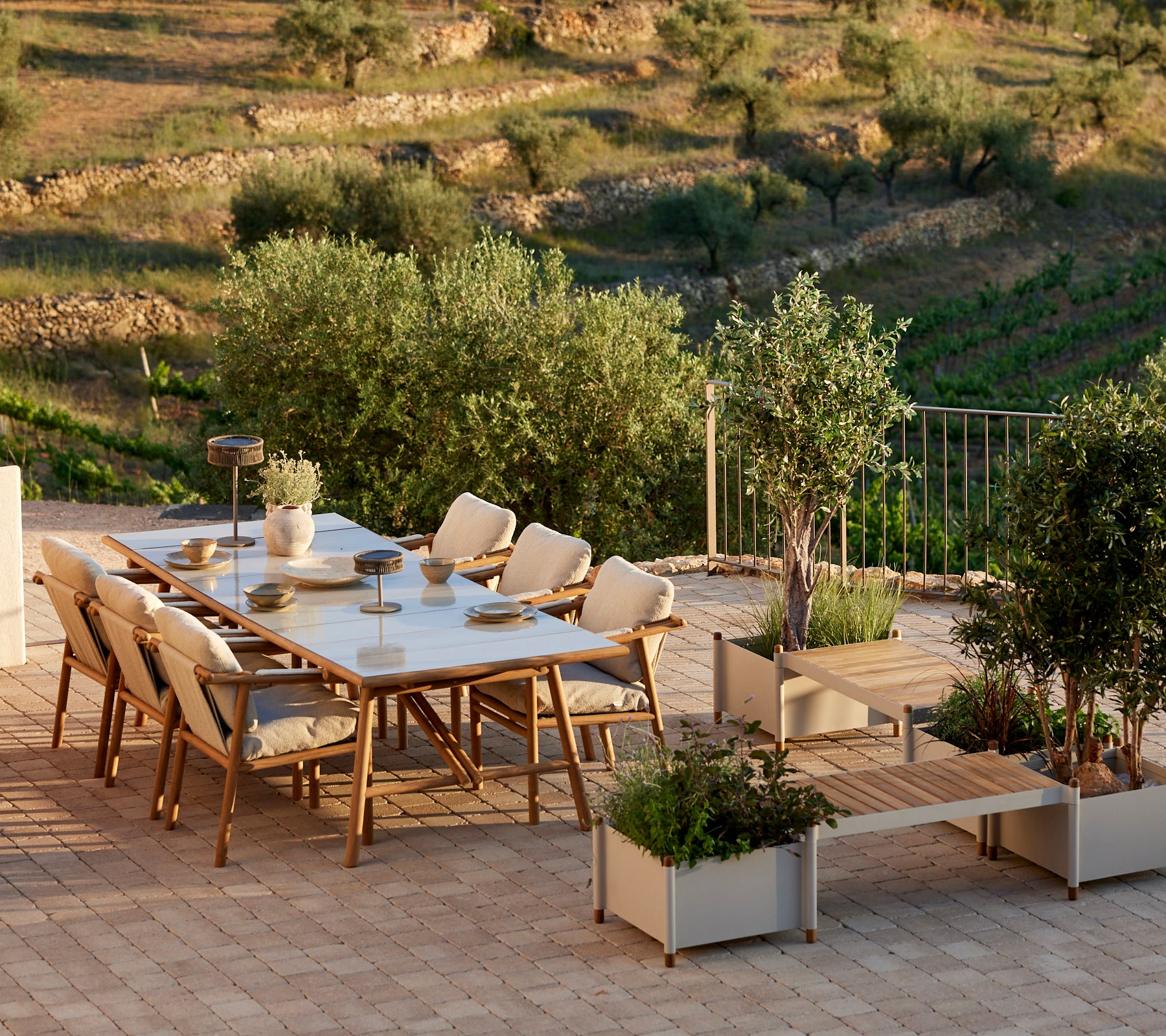 Ein stilvolles Esszimmer-Set mit Teakholz-Akzenten, das bequeme Stühle und eine Pflanzenbank umfasst, umgeben von Grün.