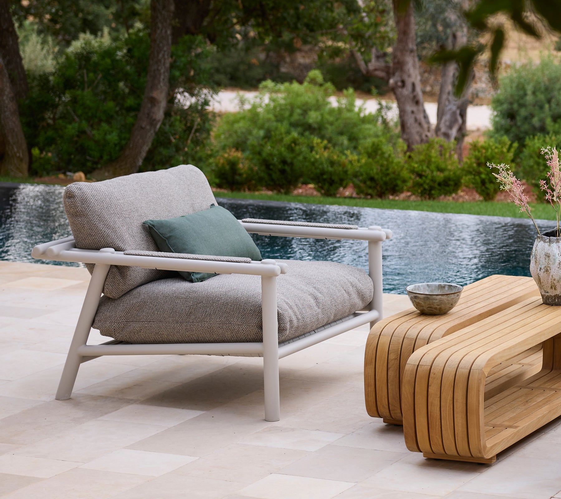 Moderne Außenbereich mit einem grauen Sofa, grünem Kissen und einem Holztisch neben einem Pool.