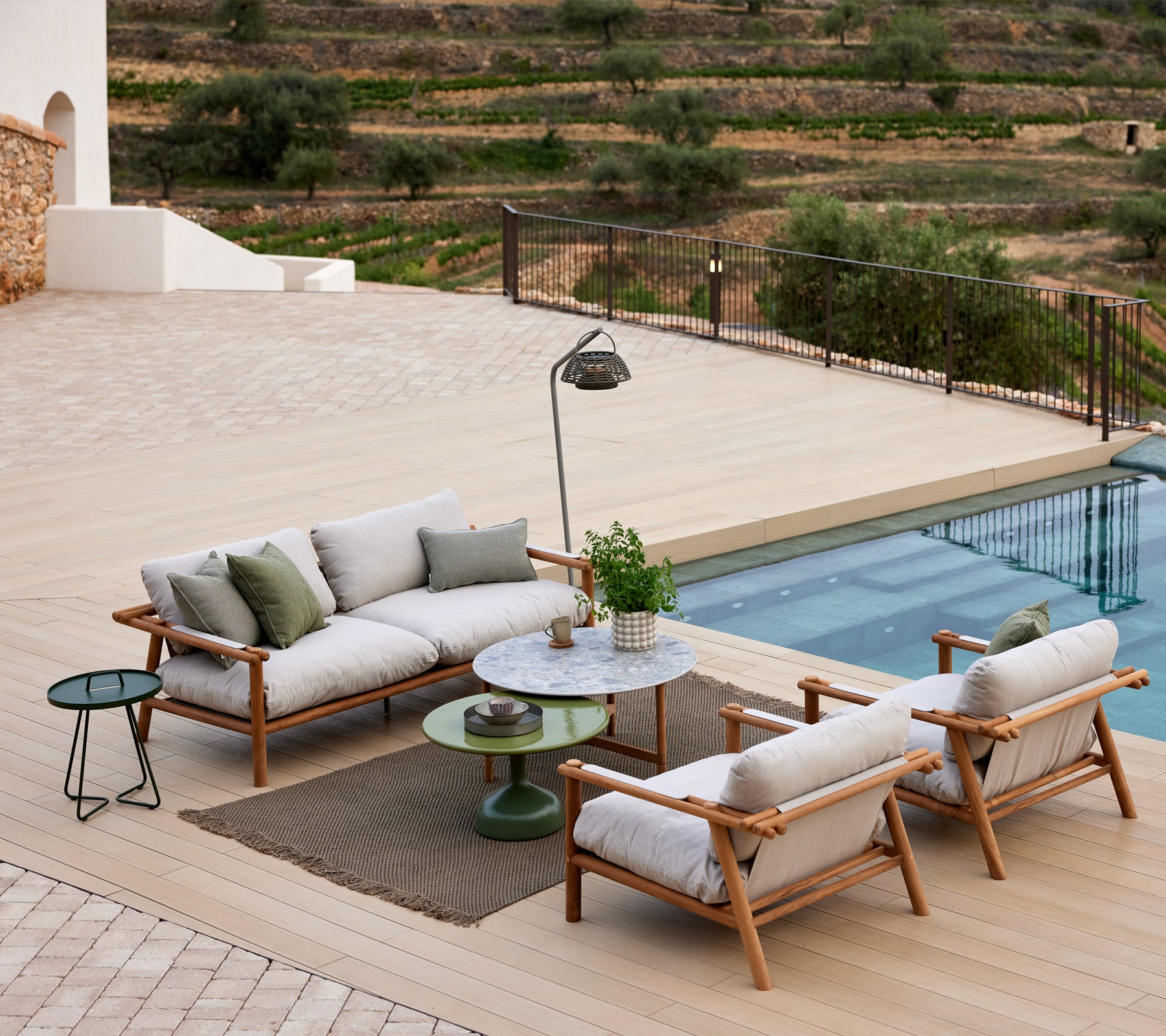 Eine Lounge-Garnitur mit Teakholzstäben, bezogen mit Strickstoff, neben einem glasierten Tisch, umgeben von einer ruhigen Landschaft.