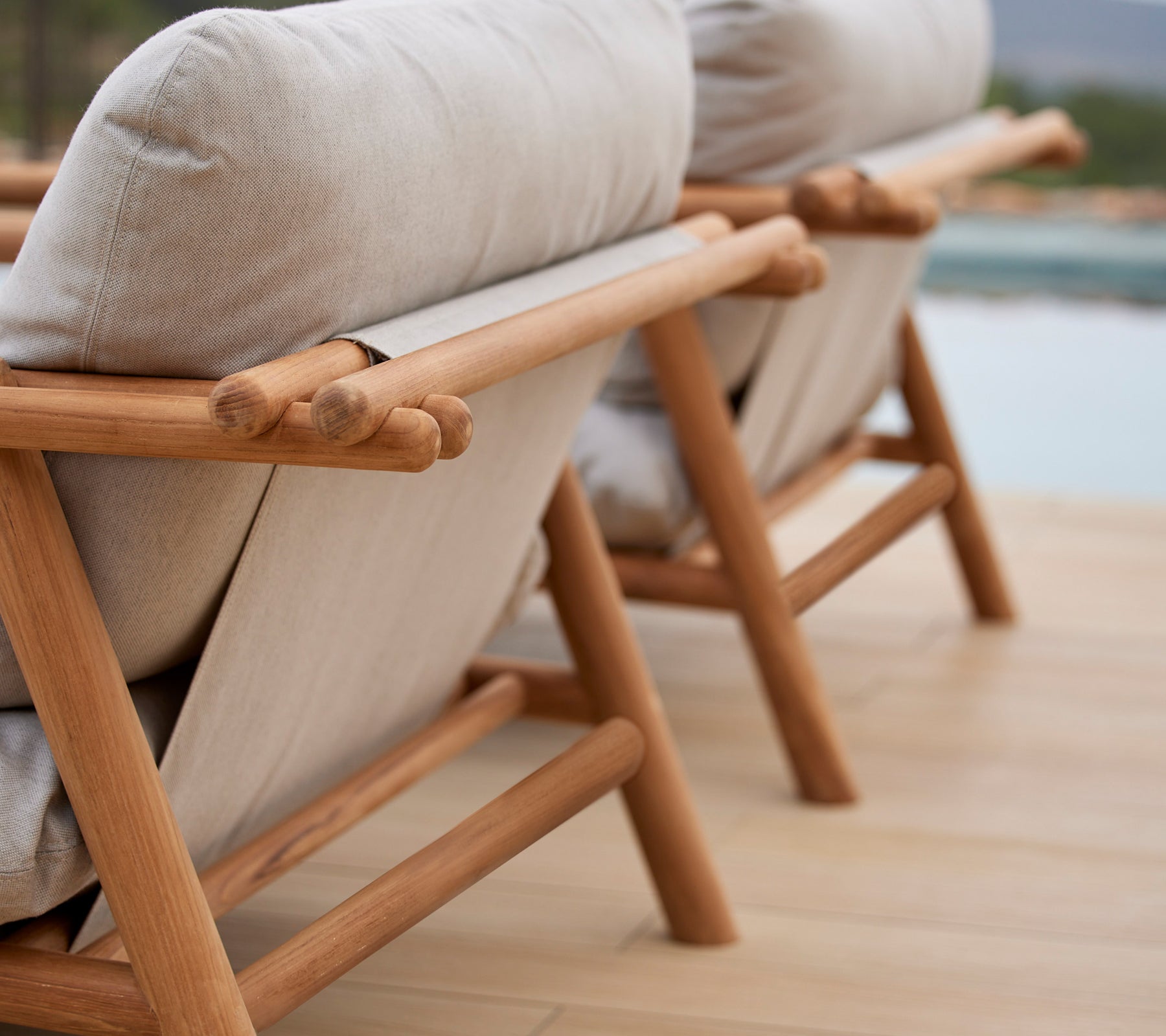 Zwei stilvolle Lounge-Stühle mit Teakrahmen und bequemen beigen Kissen, die ein einzigartiges Stabdesign auf der Rückenlehne zeigen.