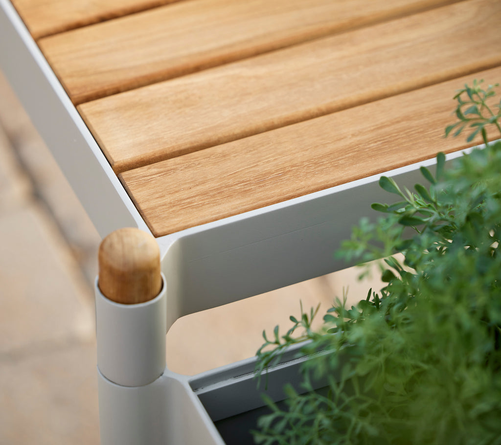 Bank mit Teaklattenoberfläche, weißem Rahmen und grünen Pflanzen, mit einem abgerundeten Holzdetaill.