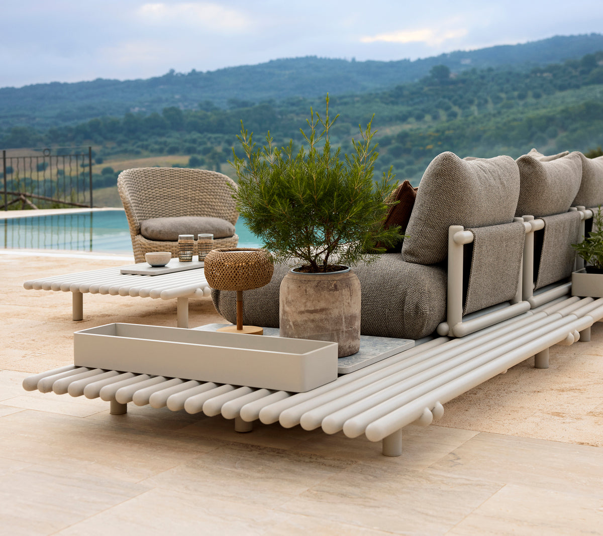Ein stilvolles Lounge-Bereich mit einem bequemen Stuhl, einer Aufbewahrungsbox und einer eleganten Plattform aus Aluminium, umgeben von Grün.
