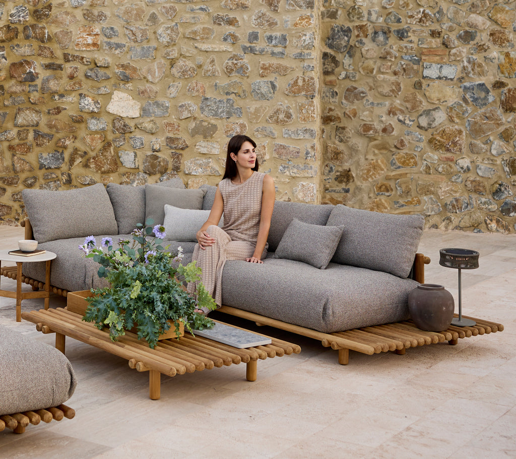 Eine elegante Ecksofa mit Kissen, begleitet von einem passenden Couchtisch, vor einer strukturierten Steinwand.
